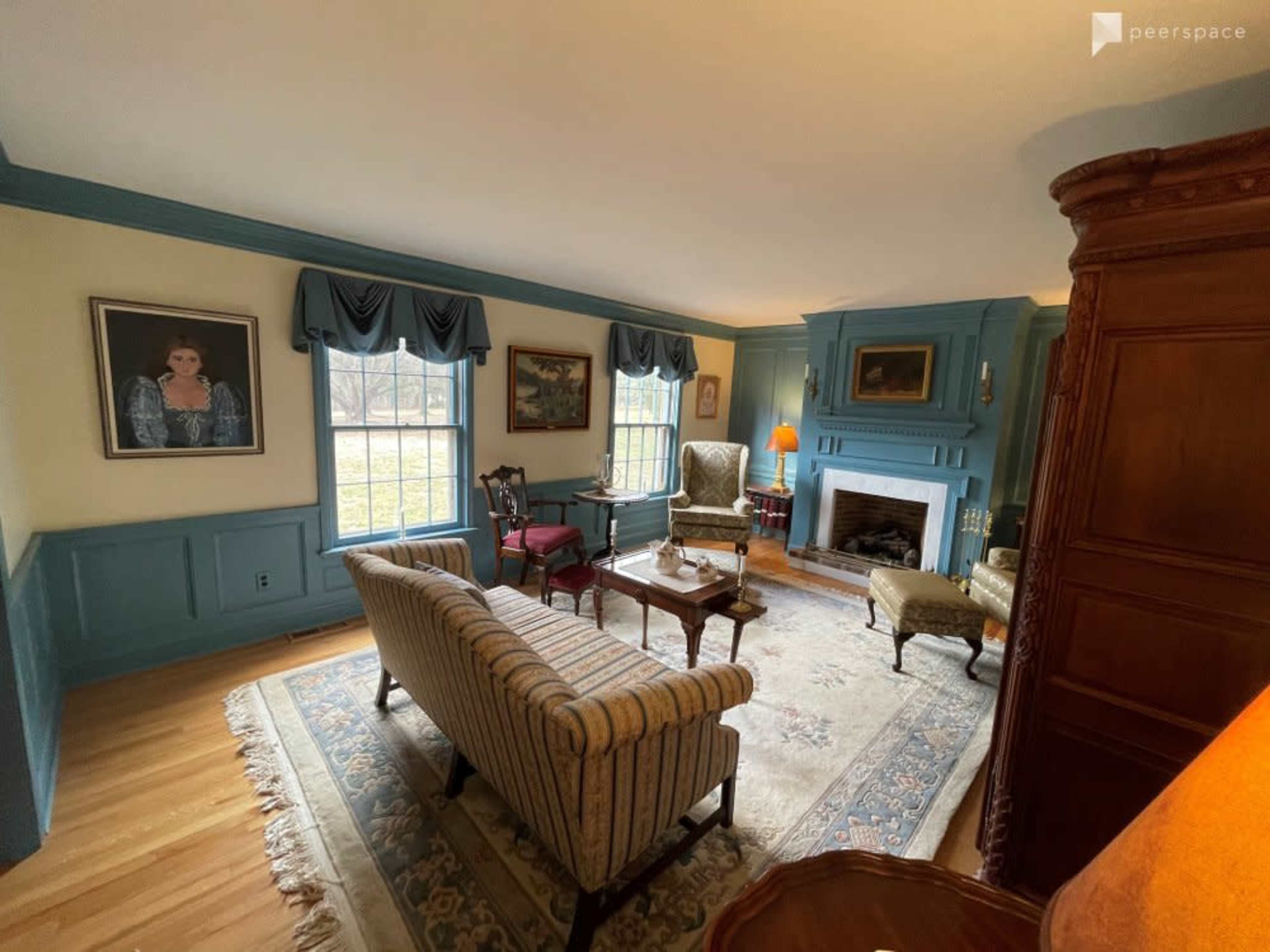 The room features a seating area with a striped sofa, two armchairs, a wooden coffee table, and a fireplace, all set against blue-paneled walls.