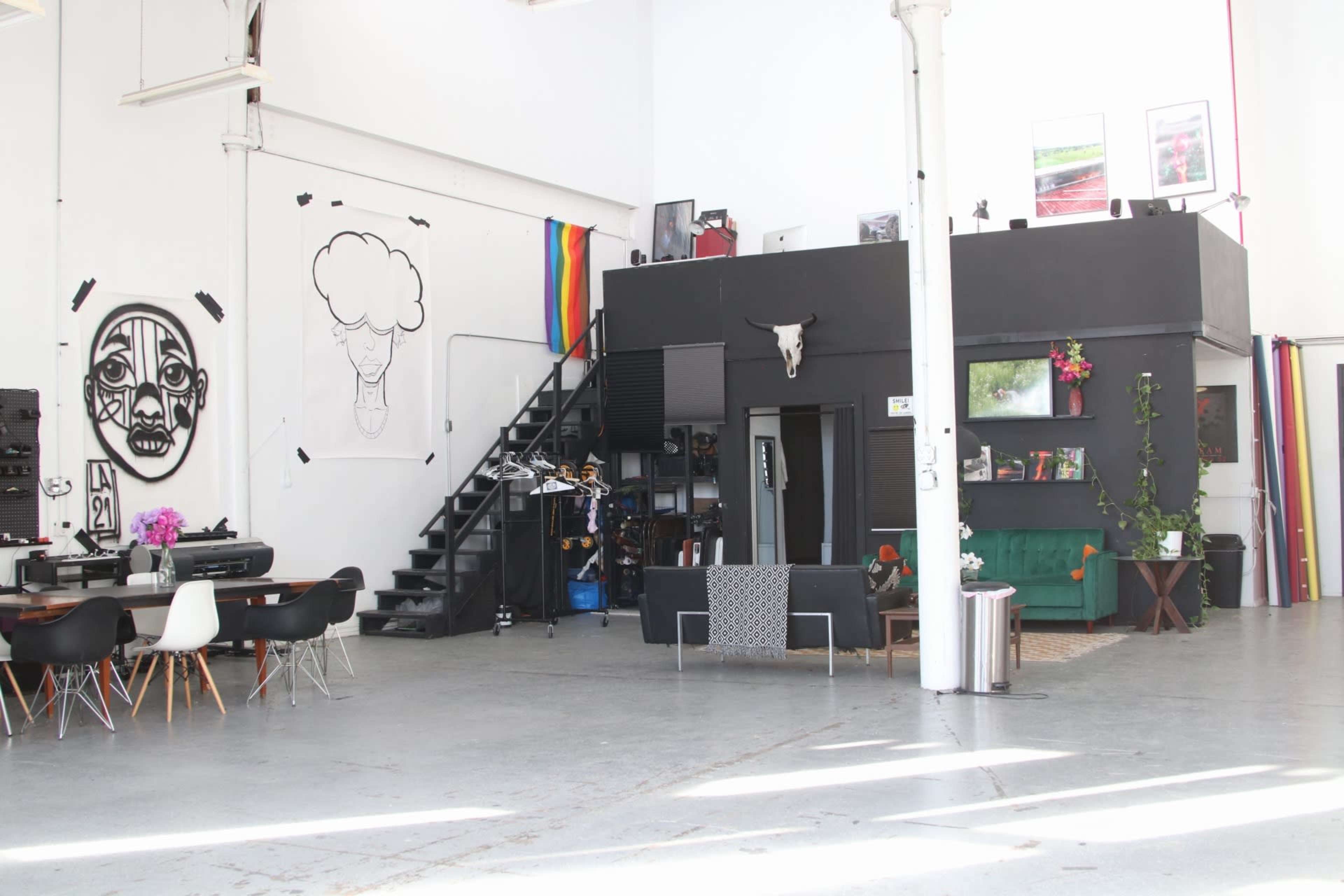 The image shows a spacious, modern interior featuring a staircase, black walls with art, and a mix of dining and lounge furniture.