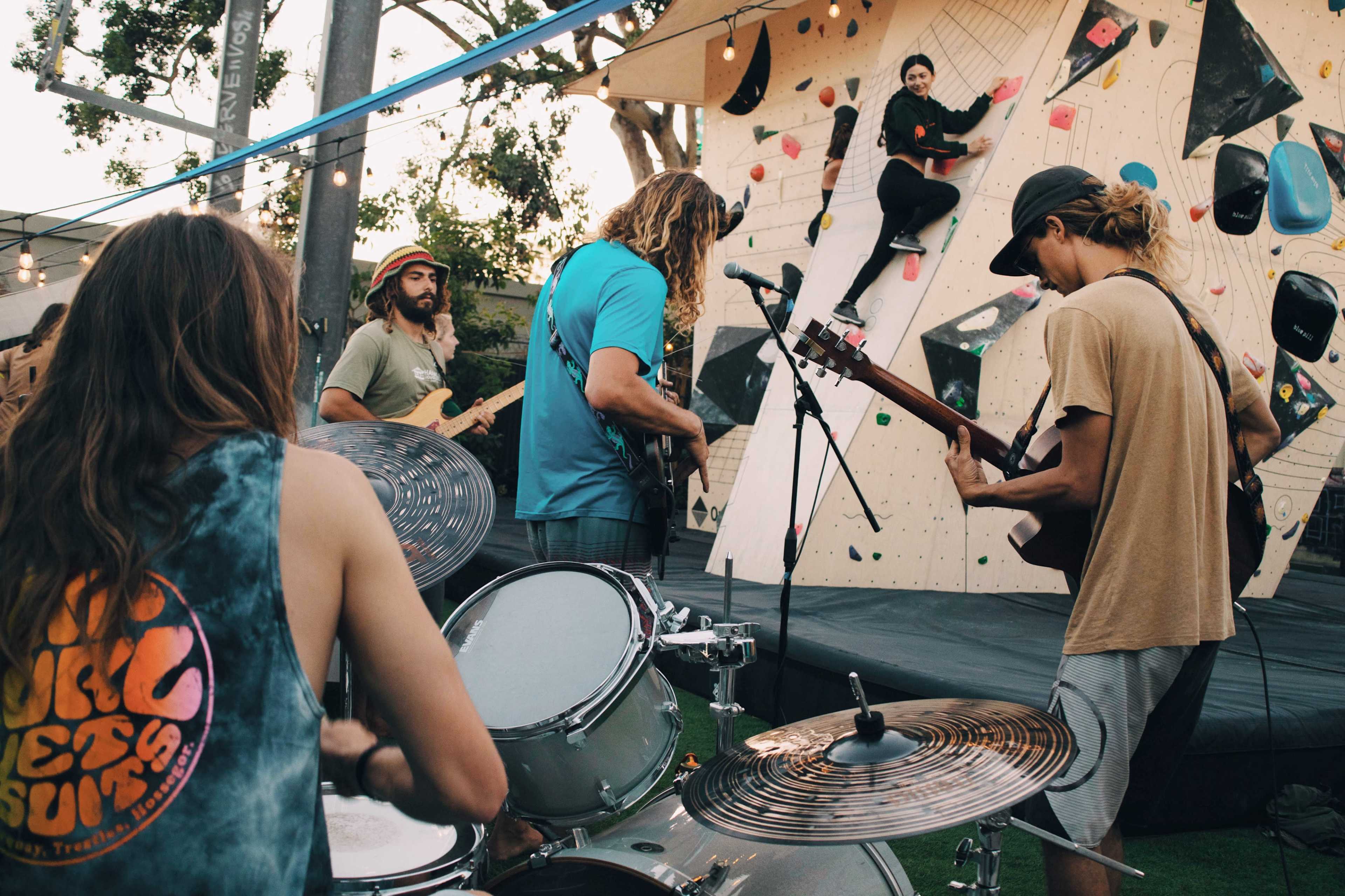 A band performs on a stage while a climber ascends an outdoor rock climbing wall.