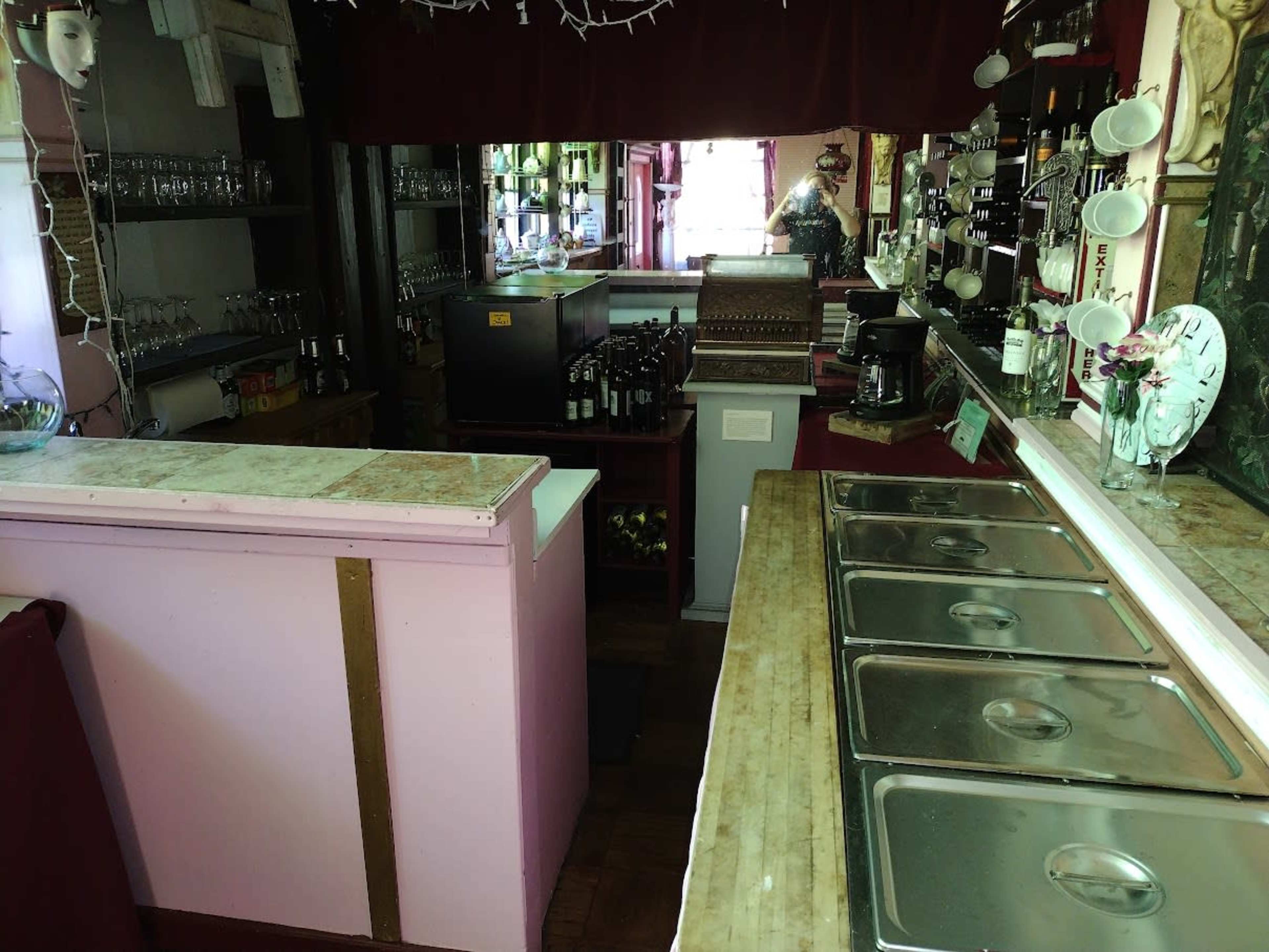 The image shows the interior of a small bar with a long counter, shelves filled with bottles, and several sinks lined along the wall.