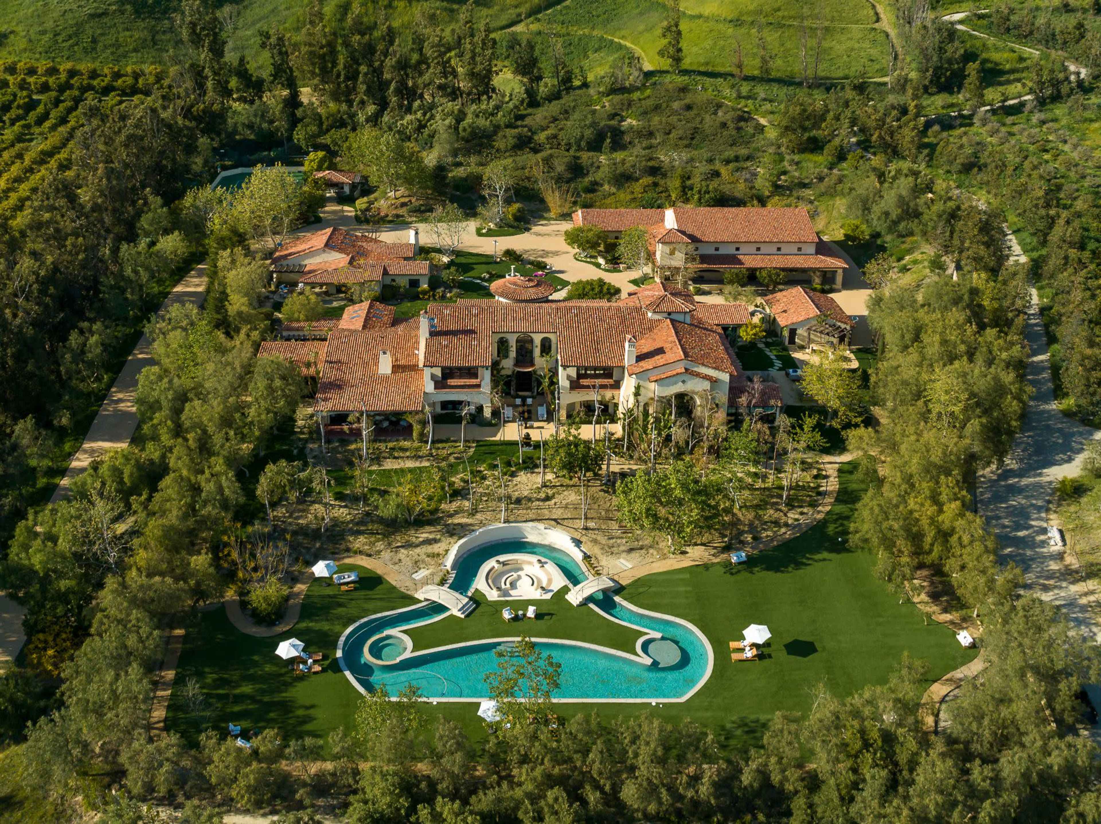 An aerial view of a large estate featuring several buildings, a landscaped lawn, and a swimming pool.