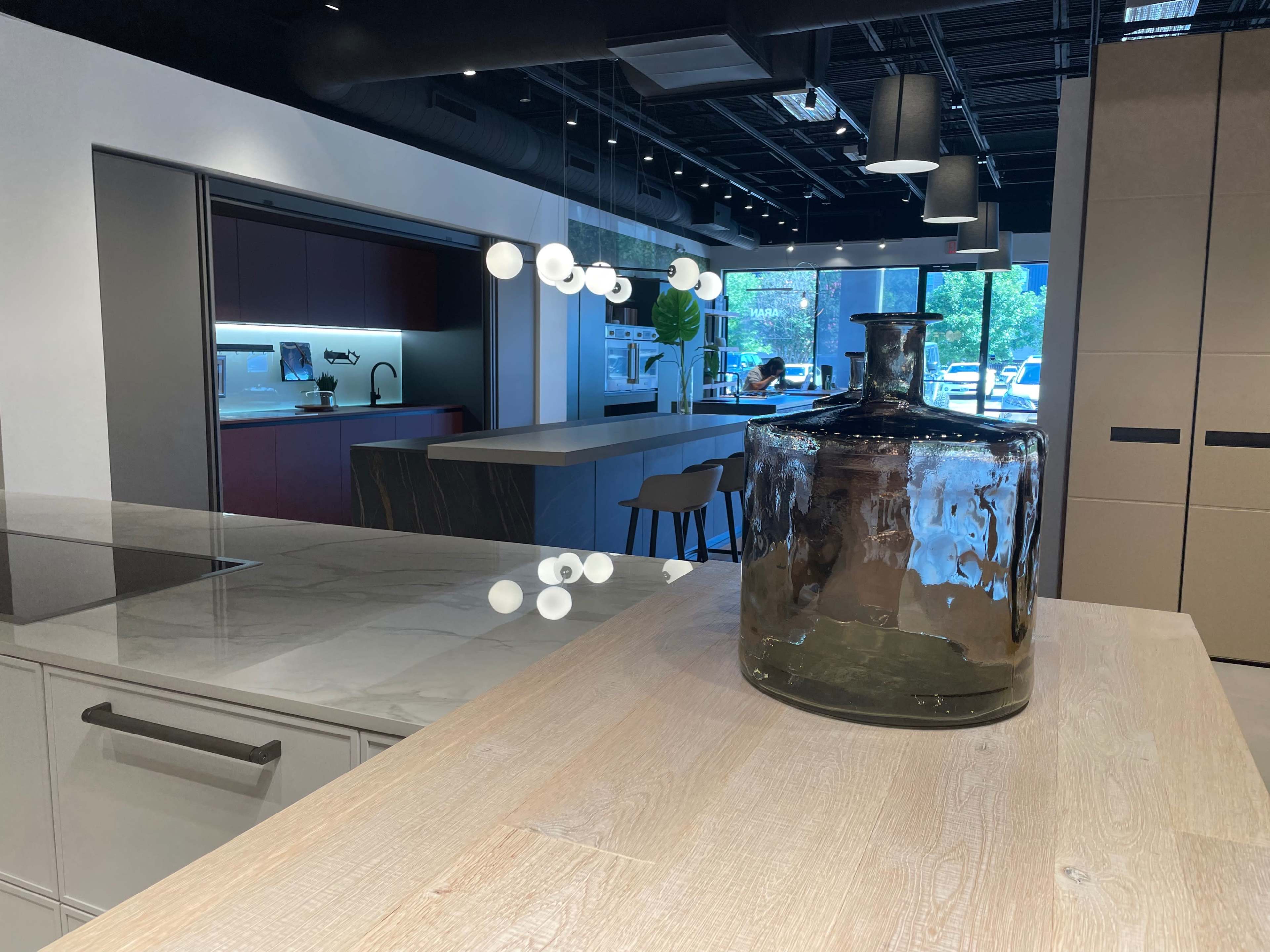 A modern kitchen display with a large glass jar on a wooden counter, featuring sleek cabinetry and a view into another room with additional kitchen features.