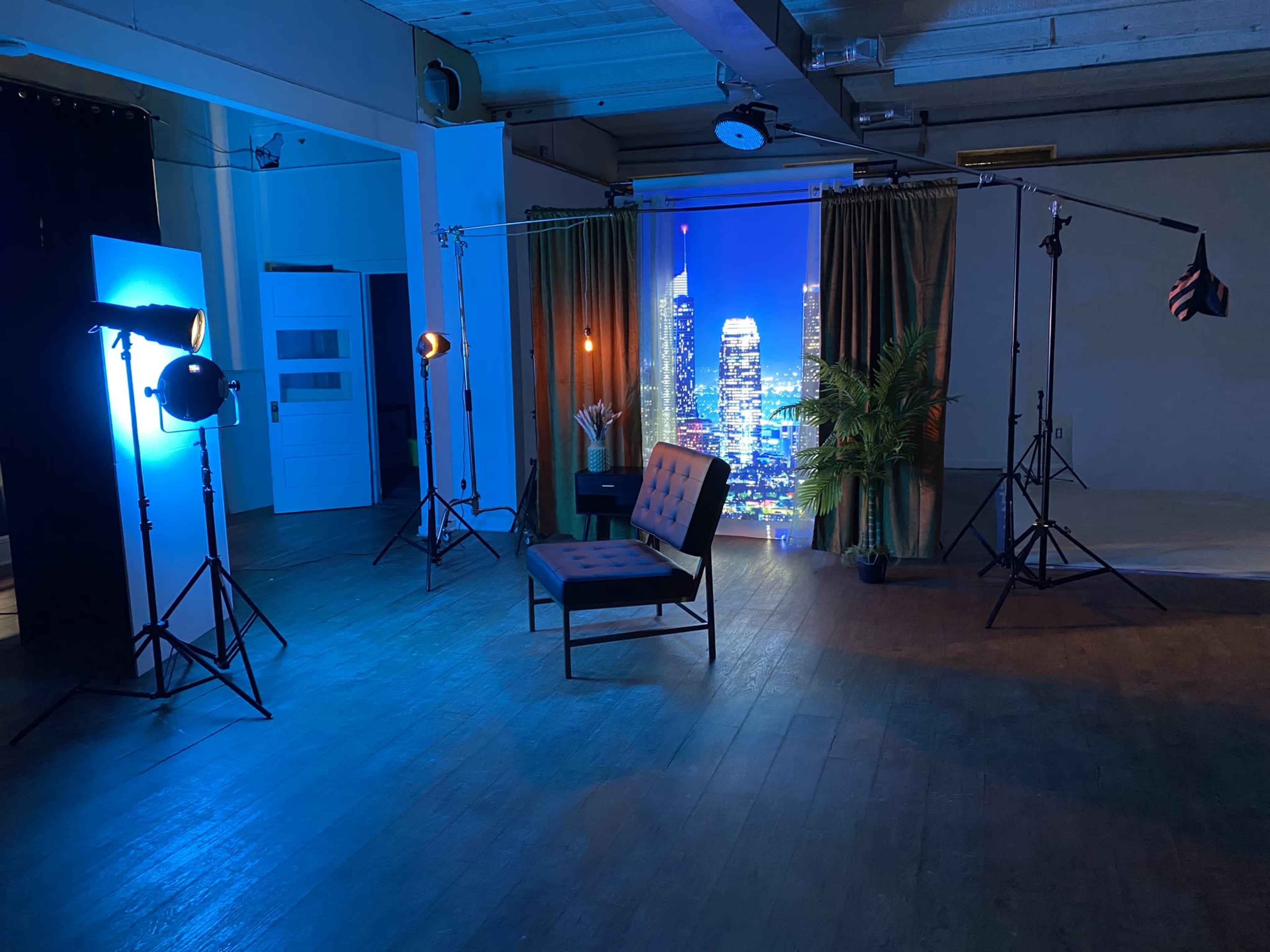 The scene shows a studio setup with a black chair, lighting equipment, and a backdrop featuring a city skyline.