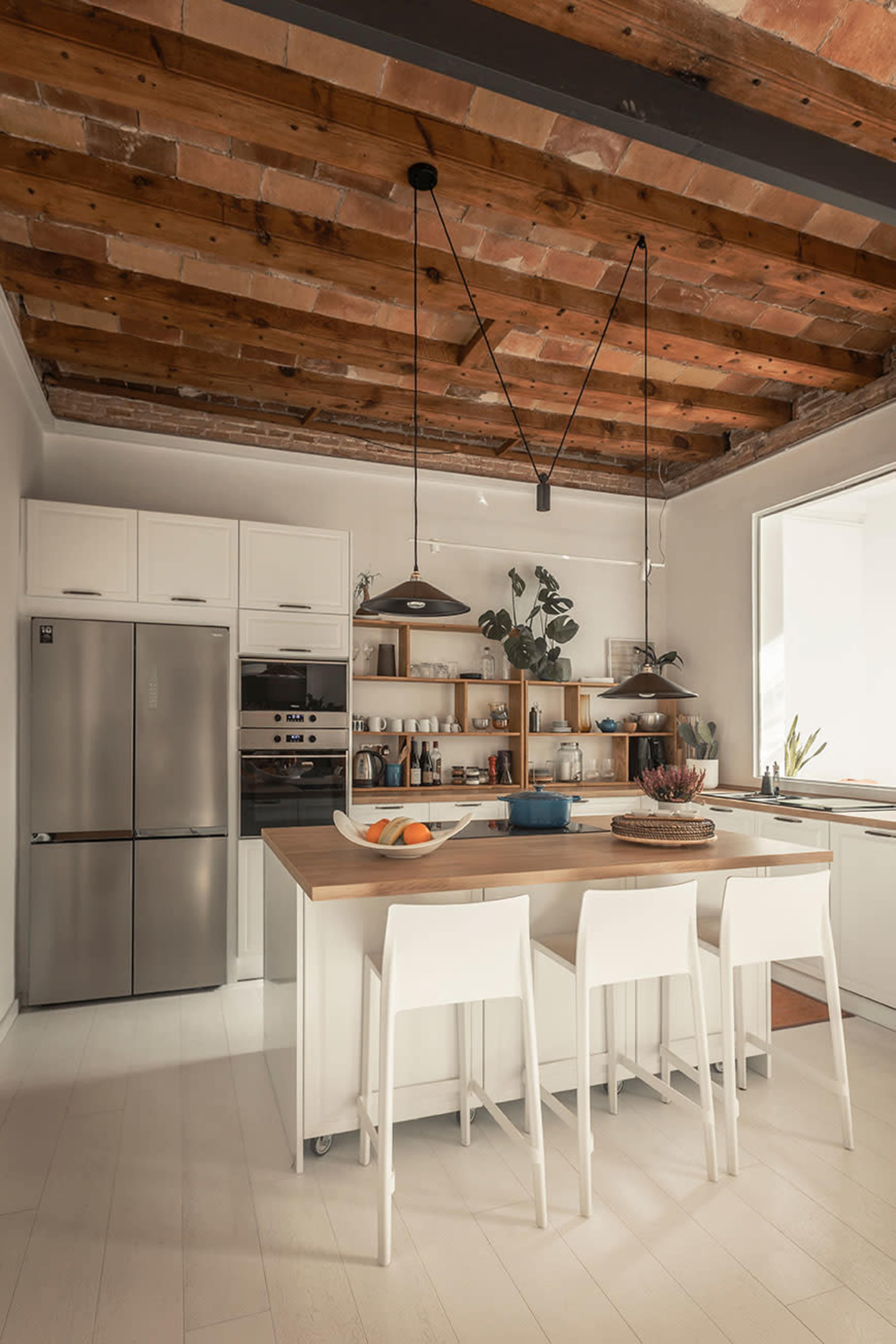 The kitchen features a central island with seating, stainless steel appliances, and wooden ceiling beams.