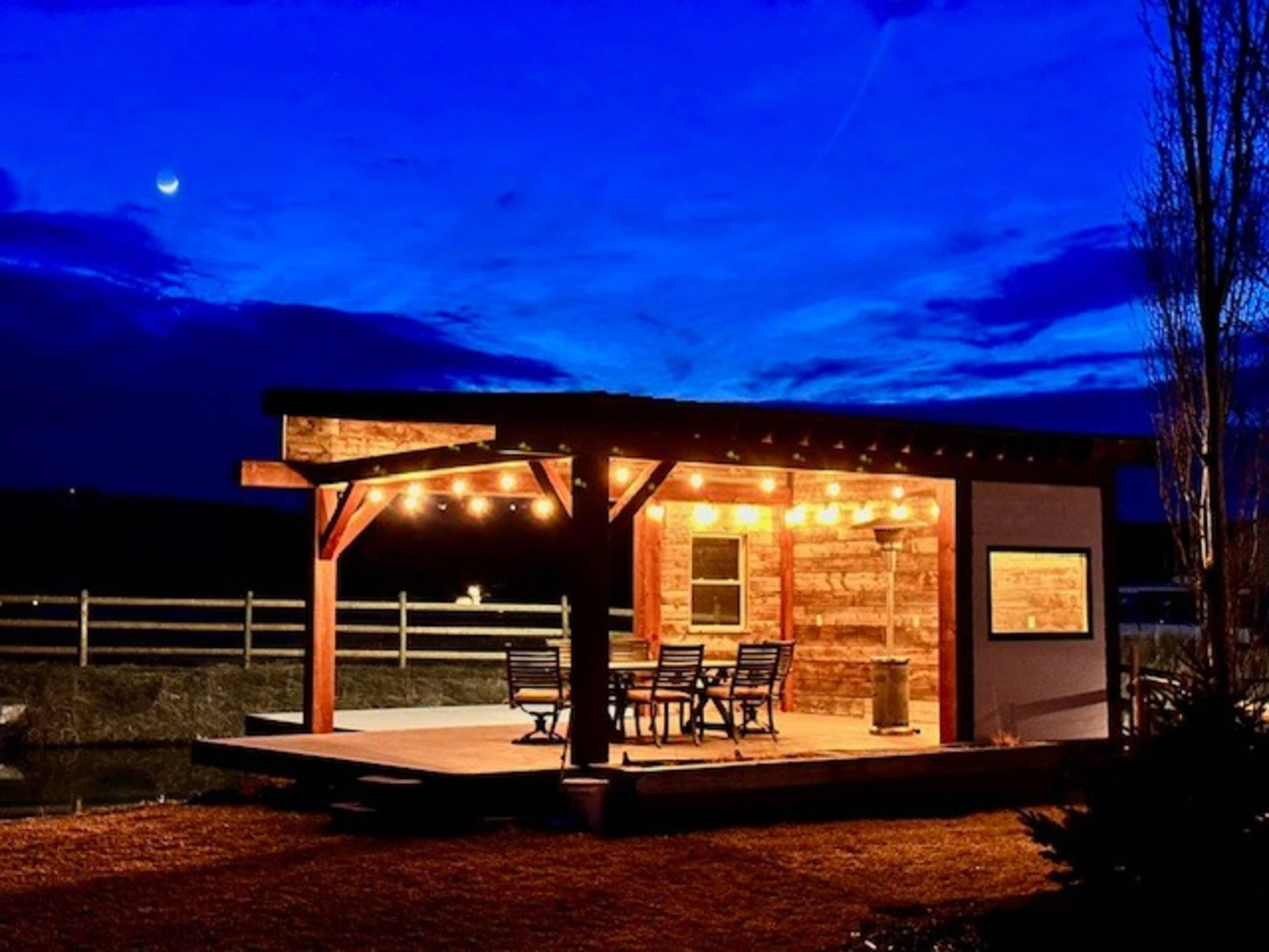 A wooden gazebo with string lights is illuminated against a twilight sky.