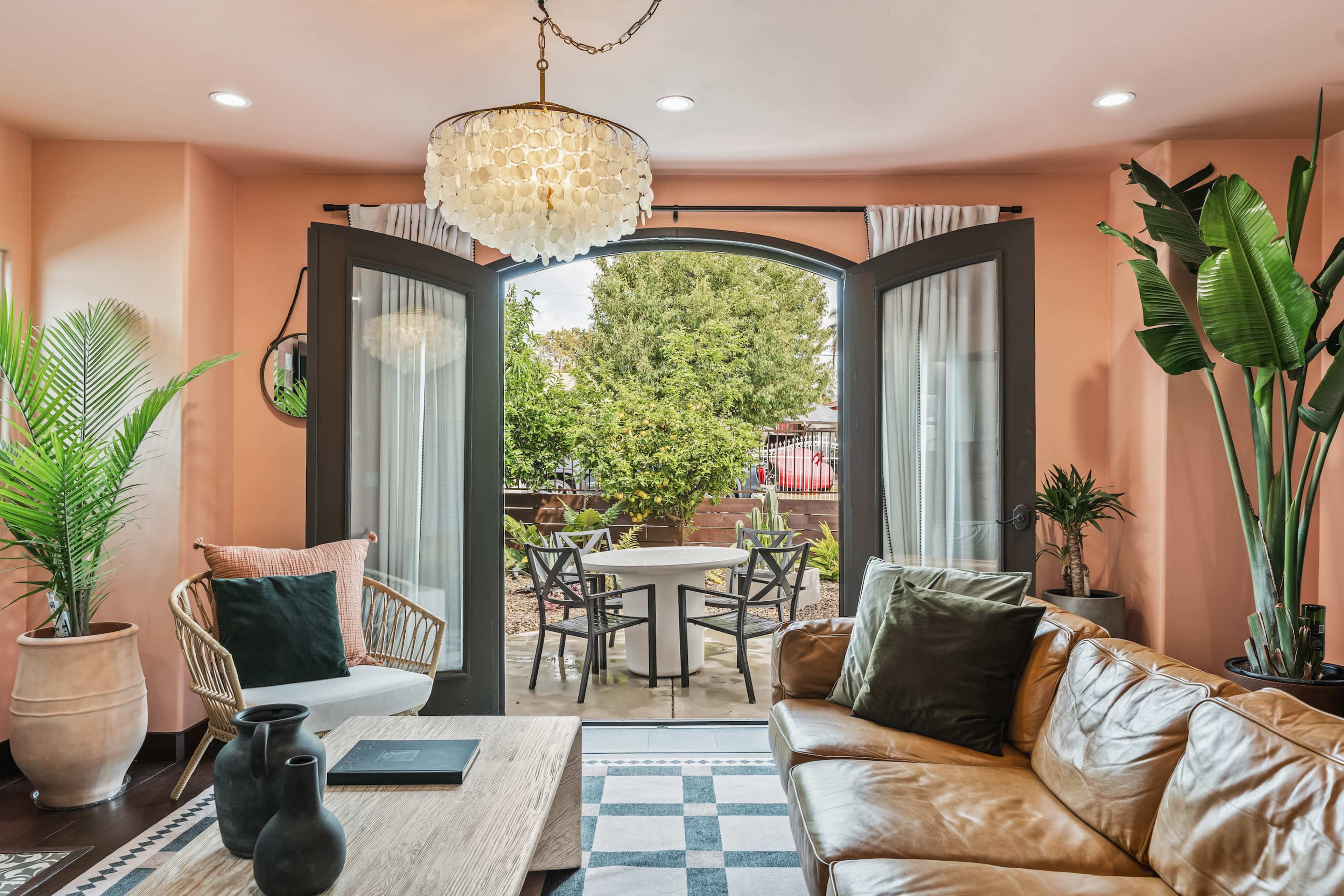 A cozy living room features a leather sofa, stylish lighting, and large open doors leading to a patio with outdoor furniture.