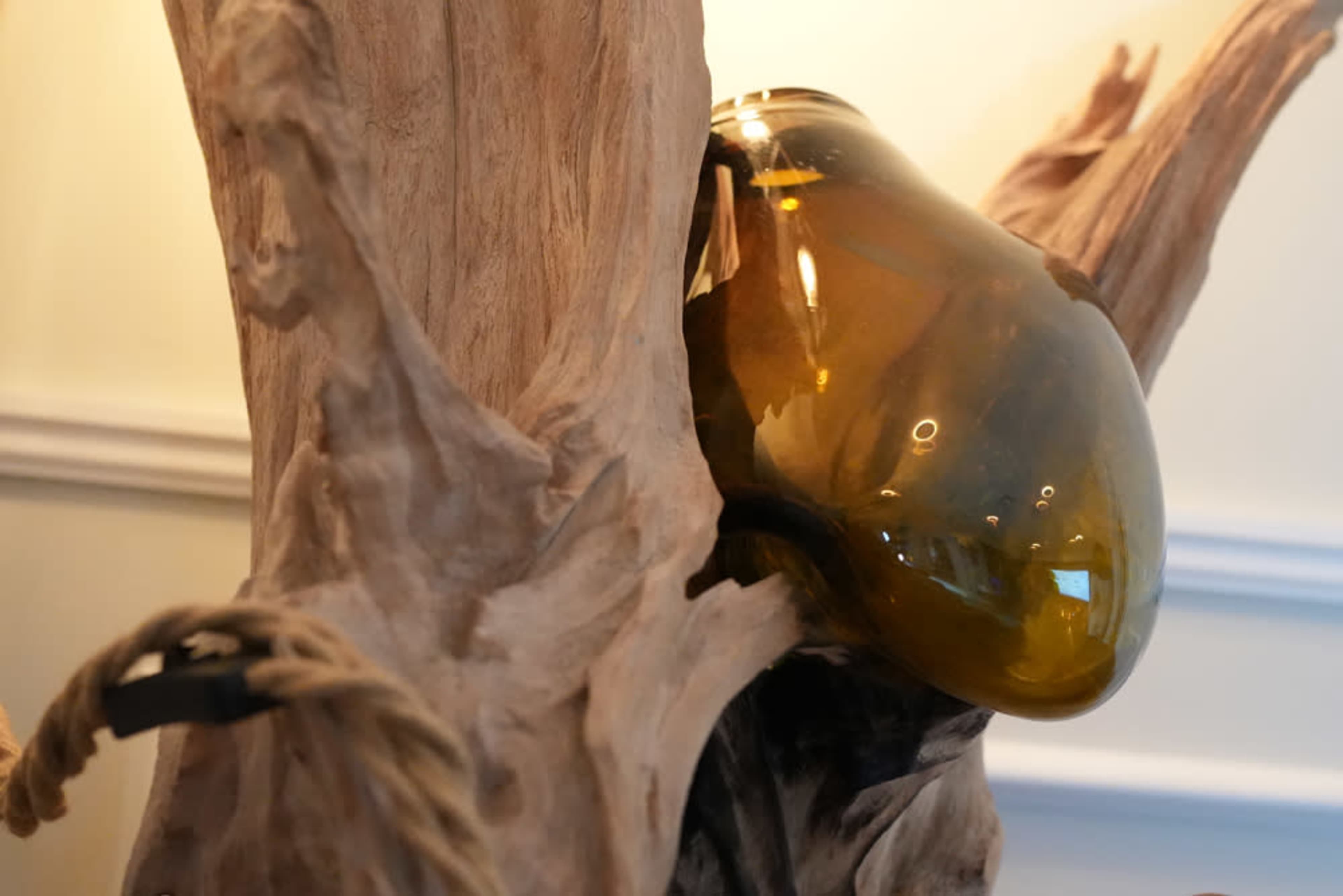 A large, amber-colored glass vase is nestled within the contours of a wooden sculpture.