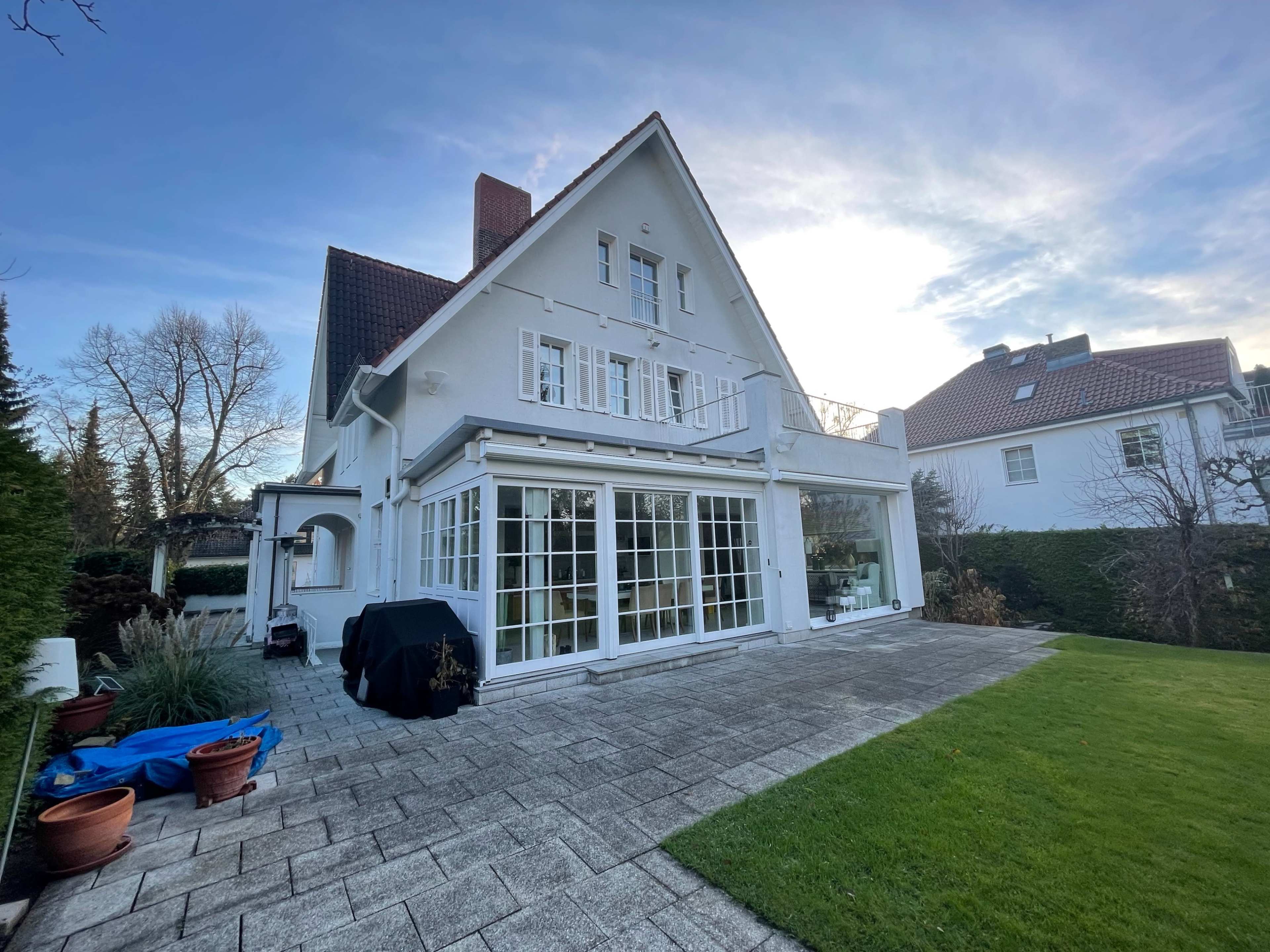 A large white house with multiple windows and a patio overlooks a neatly landscaped yard.