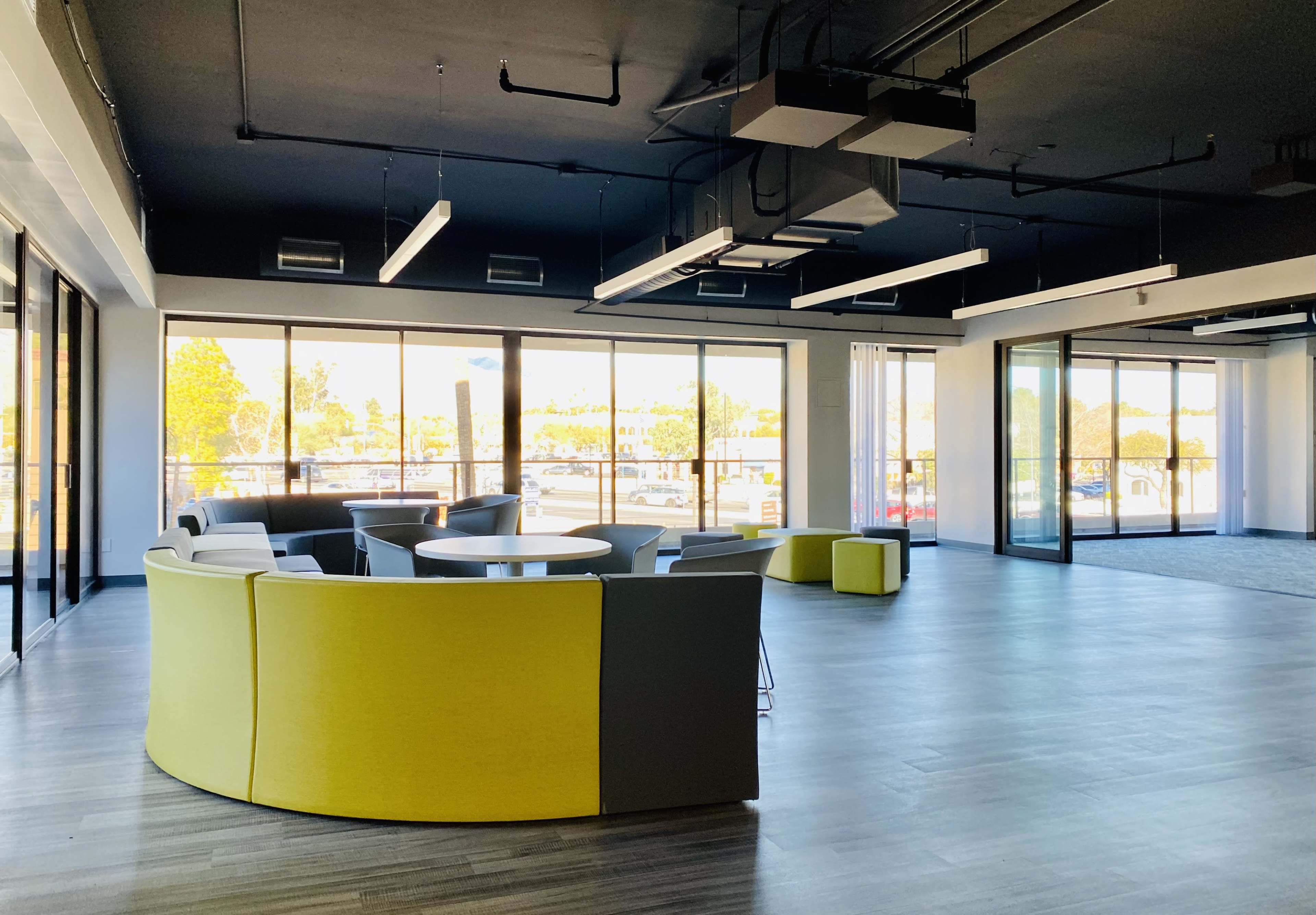 A modern office space with large windows, featuring a round table surrounded by low, colorful seating arrangements.