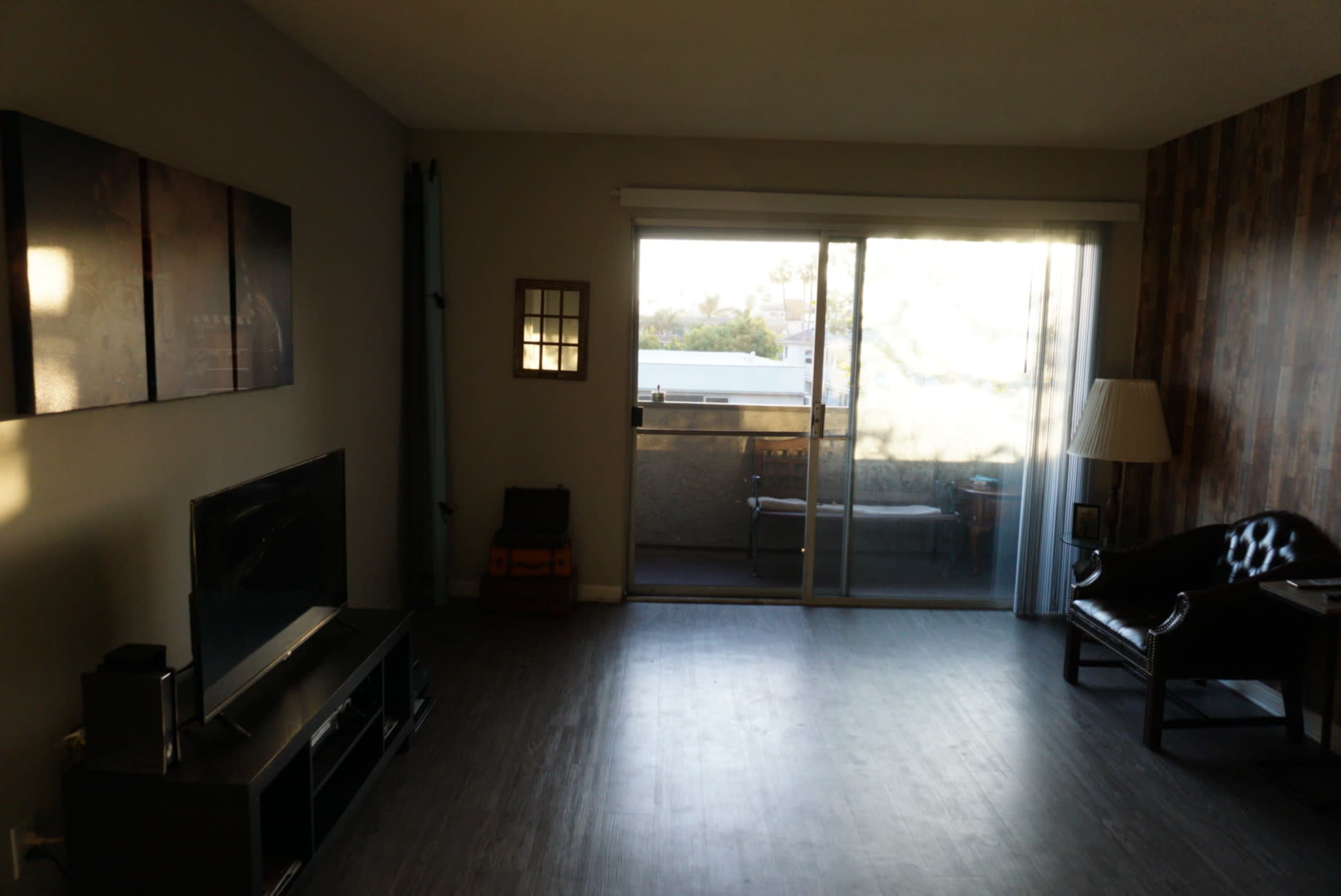 A living room with a television, a dark leather chair, and a large window allowing natural light to enter.