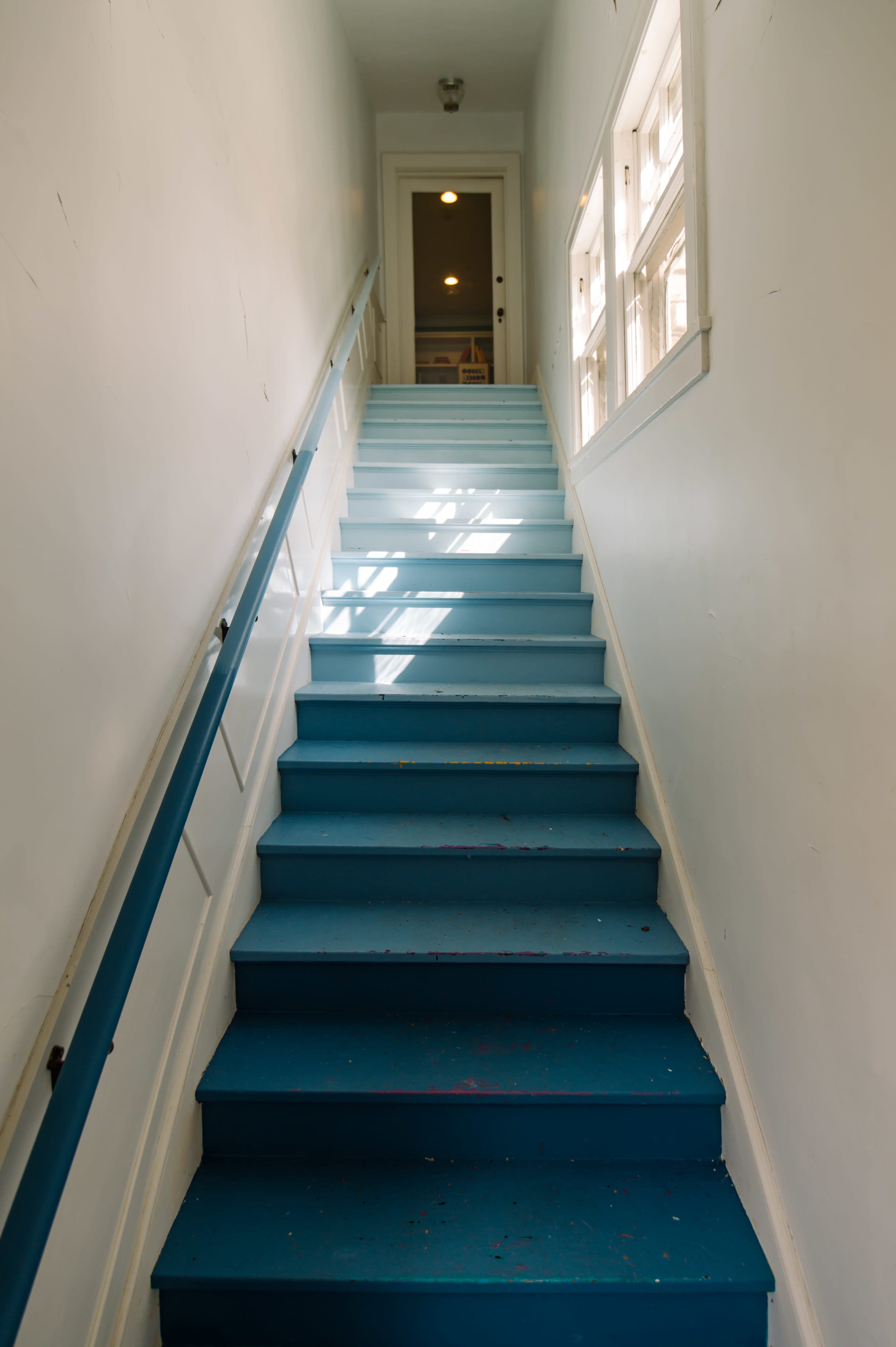 A blue staircase leads upward toward a well-lit door at the top.