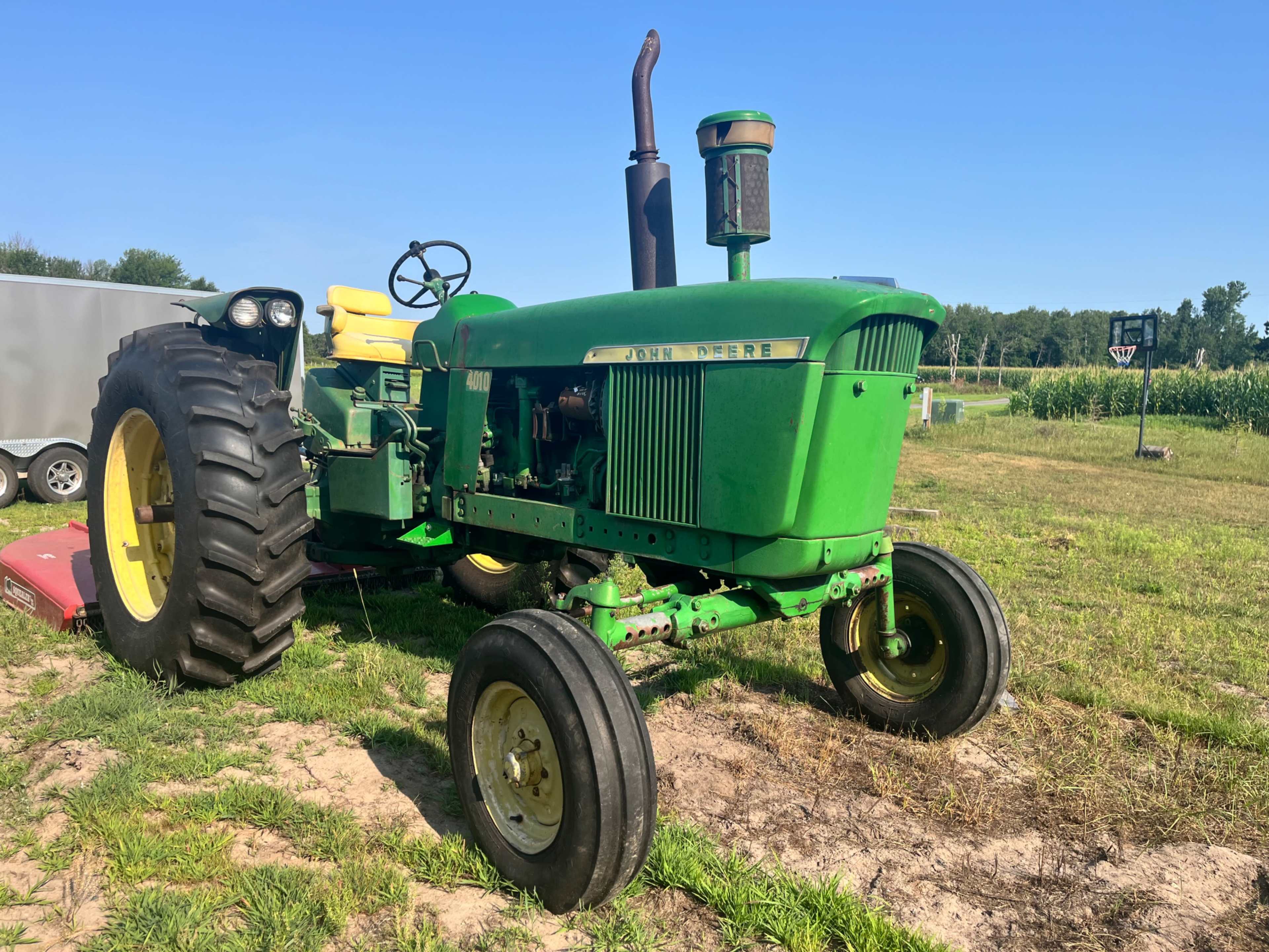 A green John Deere tractor with yellow seats is parked on a grassy field under a clear blue sky.