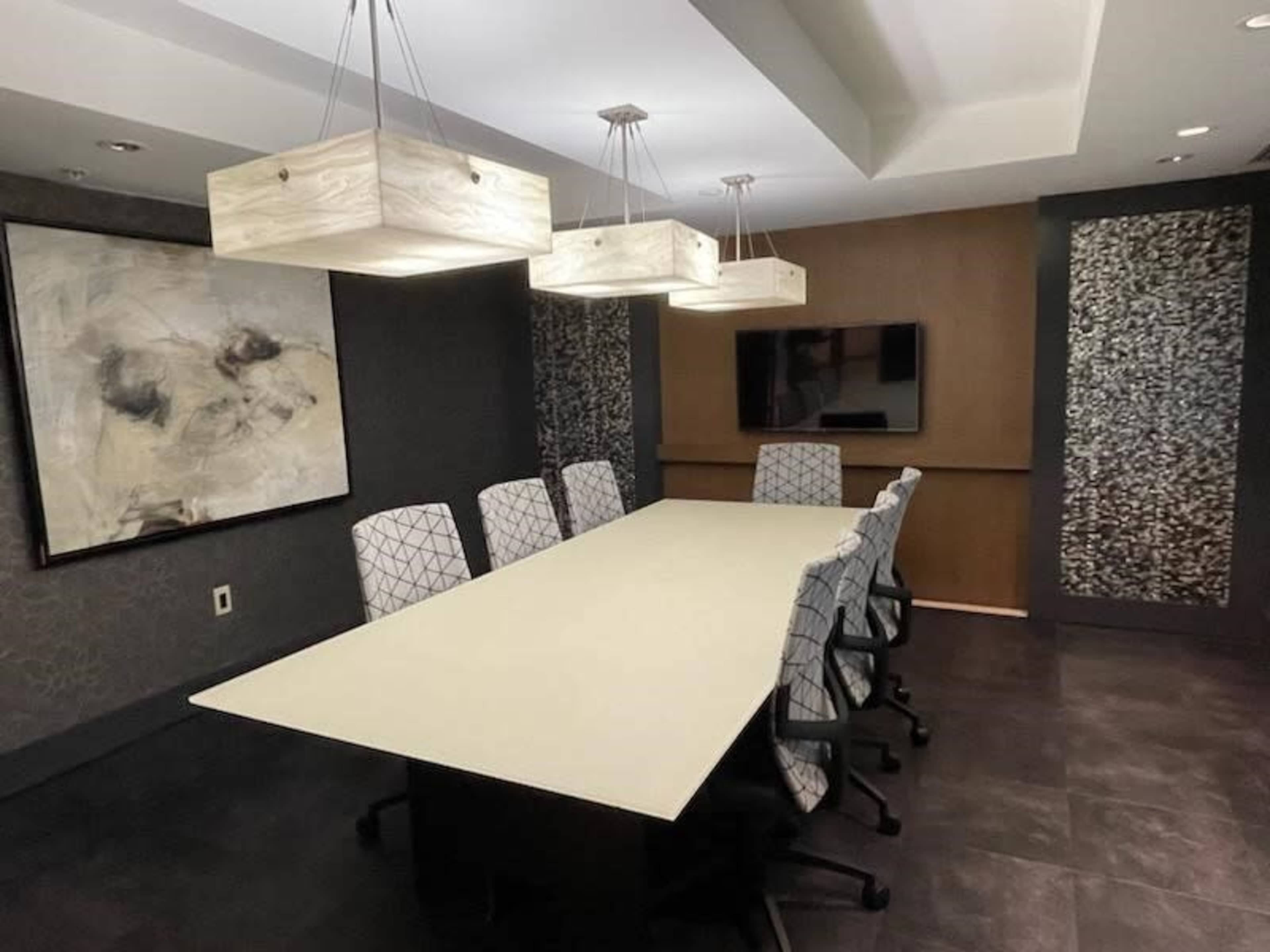 A modern conference room with a long table, six patterned chairs, and three pendant lights overhead.