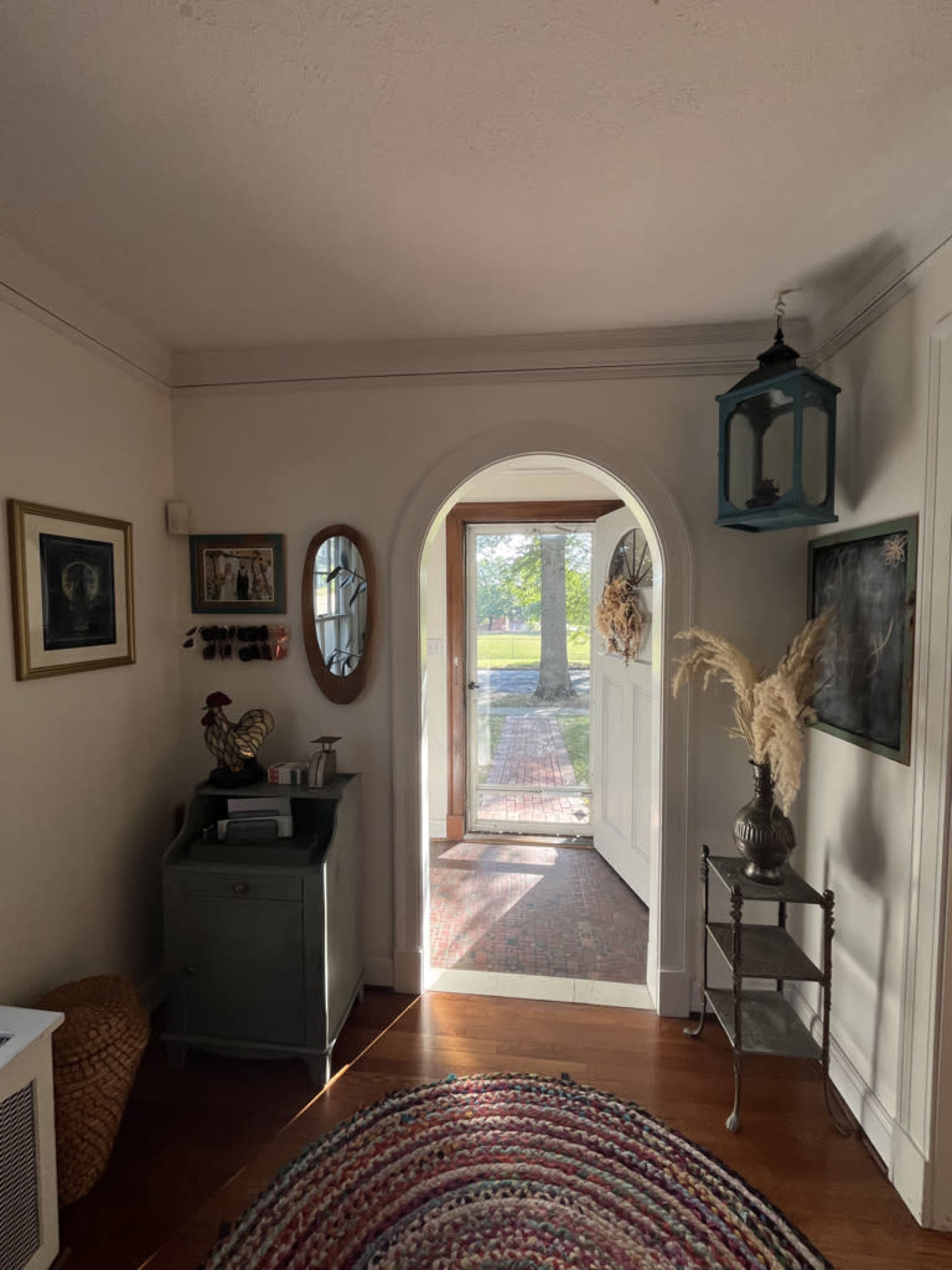 The image shows a well-lit hallway with an arched doorway leading to an outdoor view, decorated with framed pictures and a colorful rug.