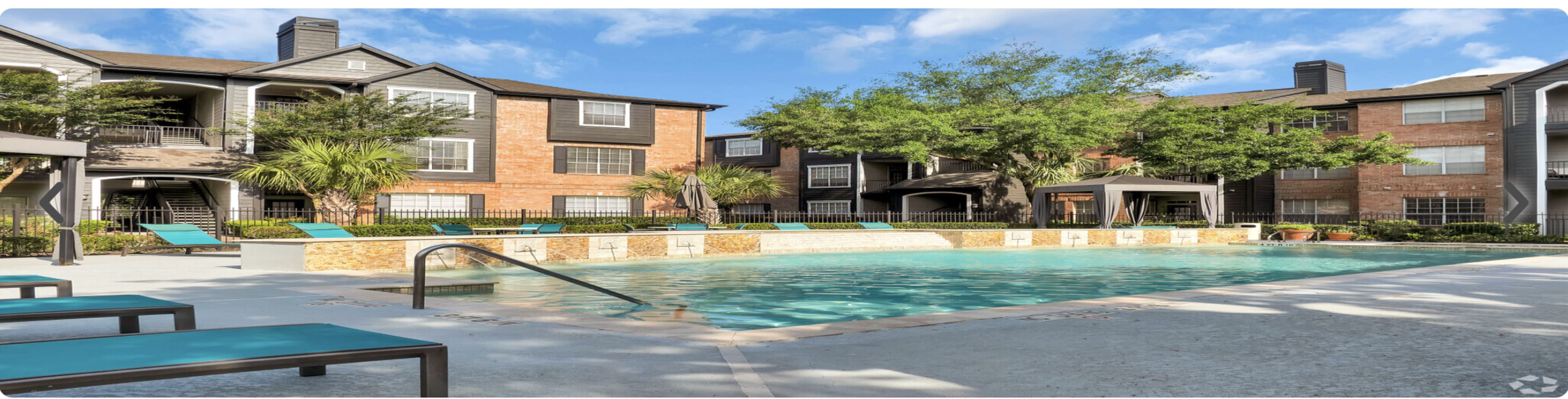 The image shows a pool area surrounded by brick apartment buildings, with lounge chairs and palm trees nearby.
