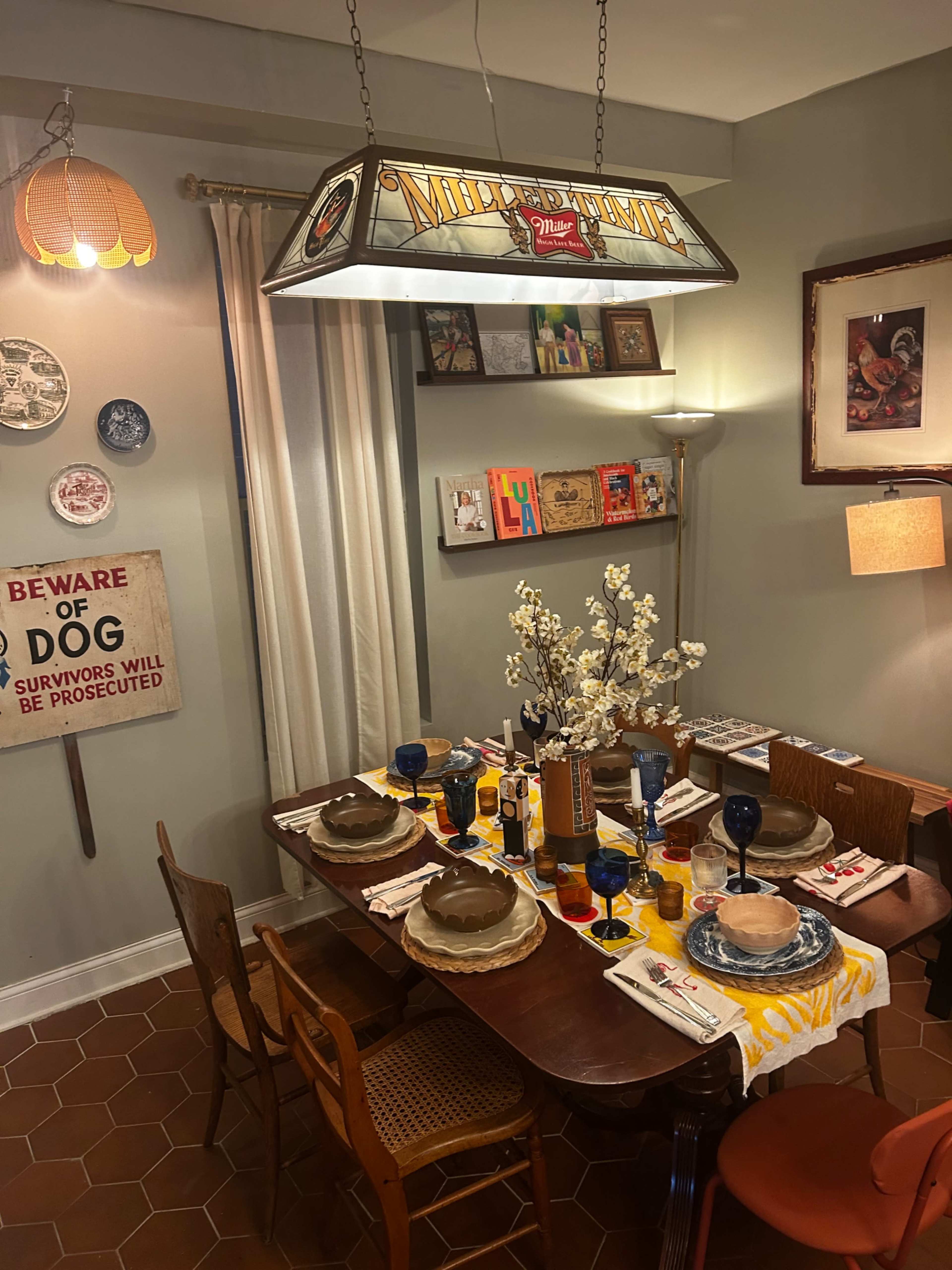 A dining room is set with a table adorned with plates, glasses, and decorative items, featuring a large stained glass light fixture overhead.