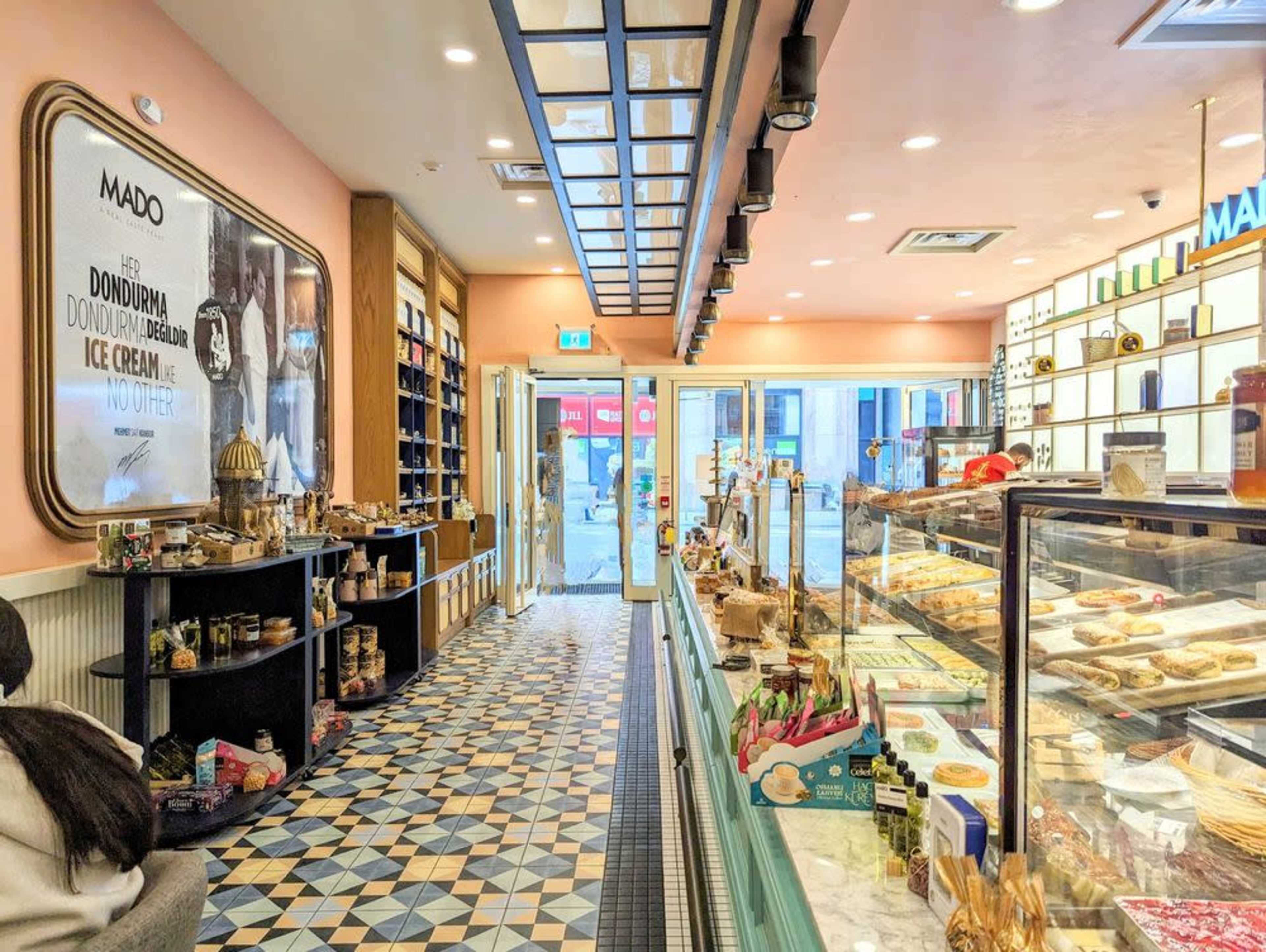 The image shows a brightly lit café interior with a display case filled with pastries and an open entrance leading to the street.