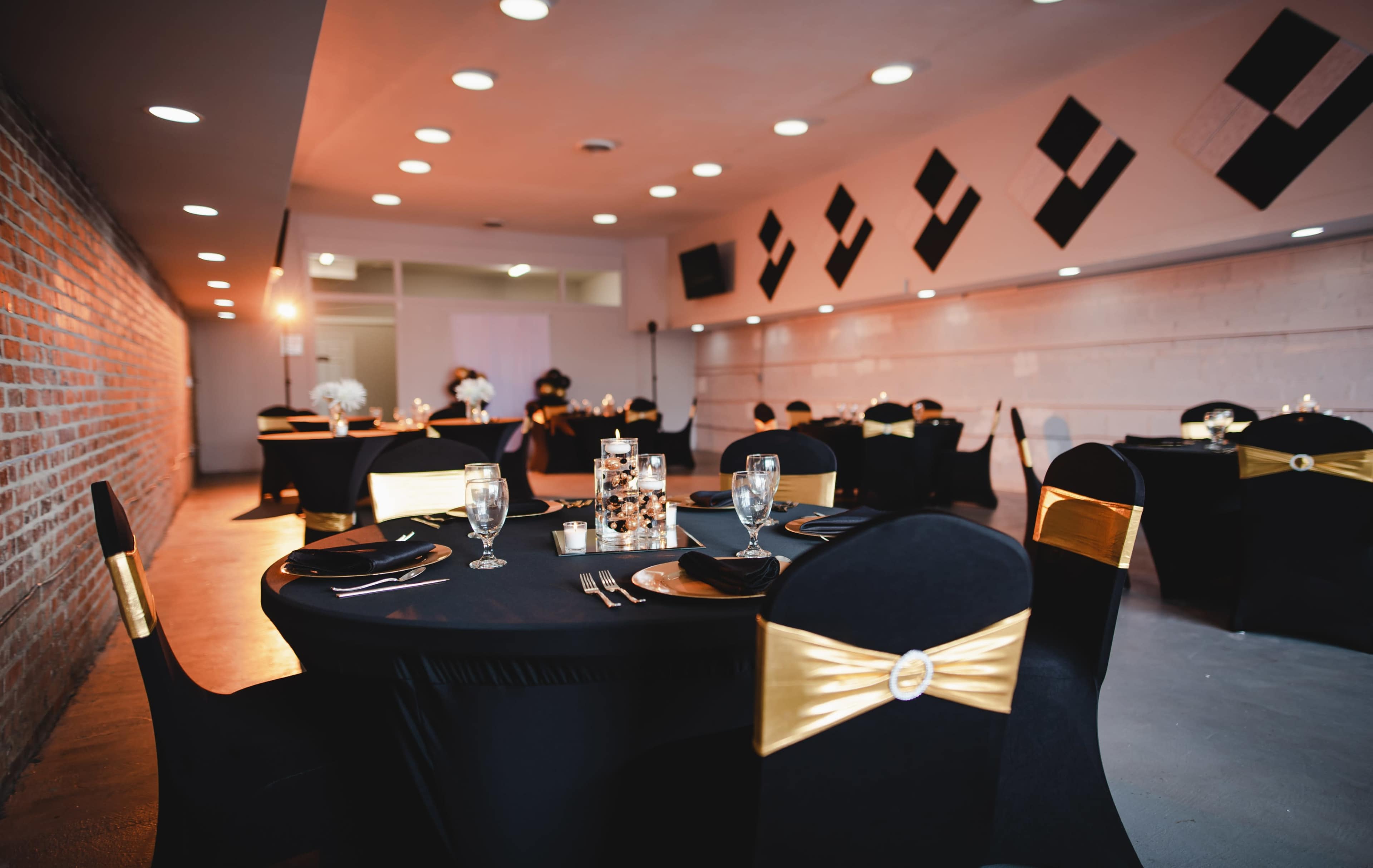 The scene shows a banquet hall set with black tables adorned with gold sashes, glassware, and decorative centerpieces.