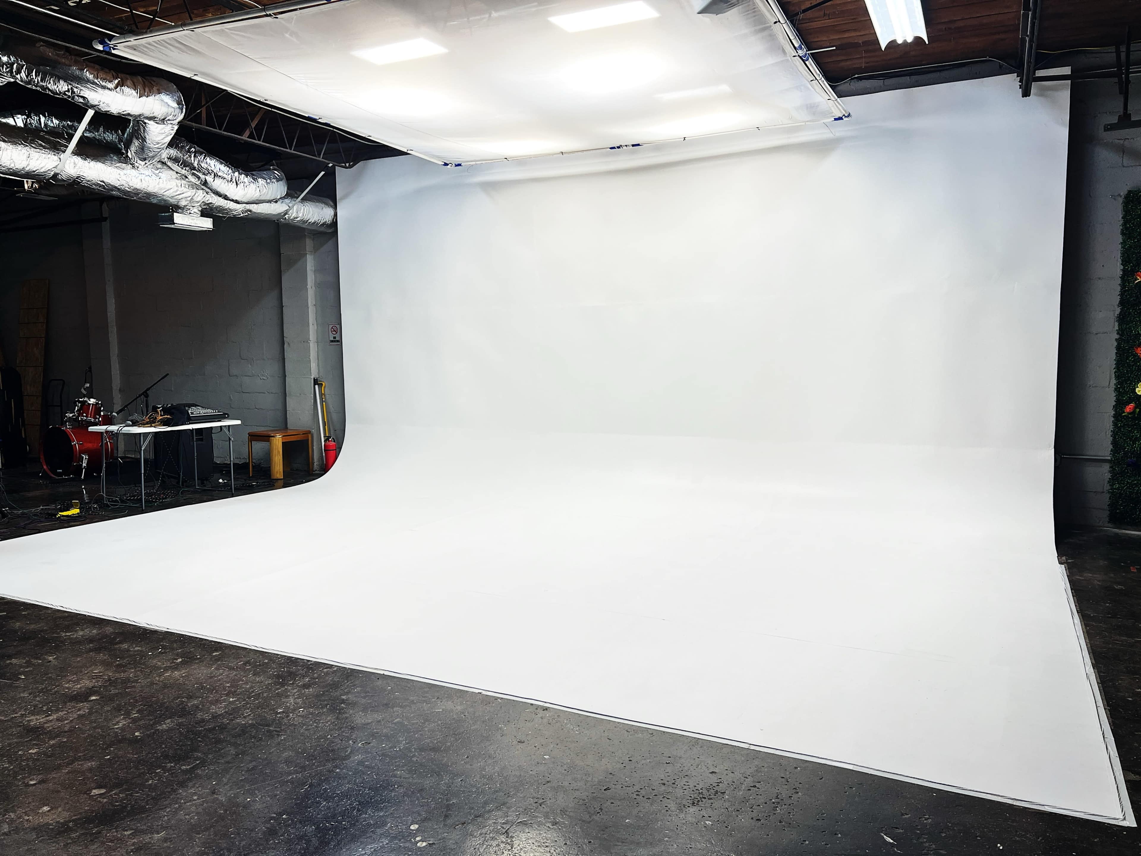 The image shows a spacious photography studio with a large, seamless white backdrop and industrial lighting.