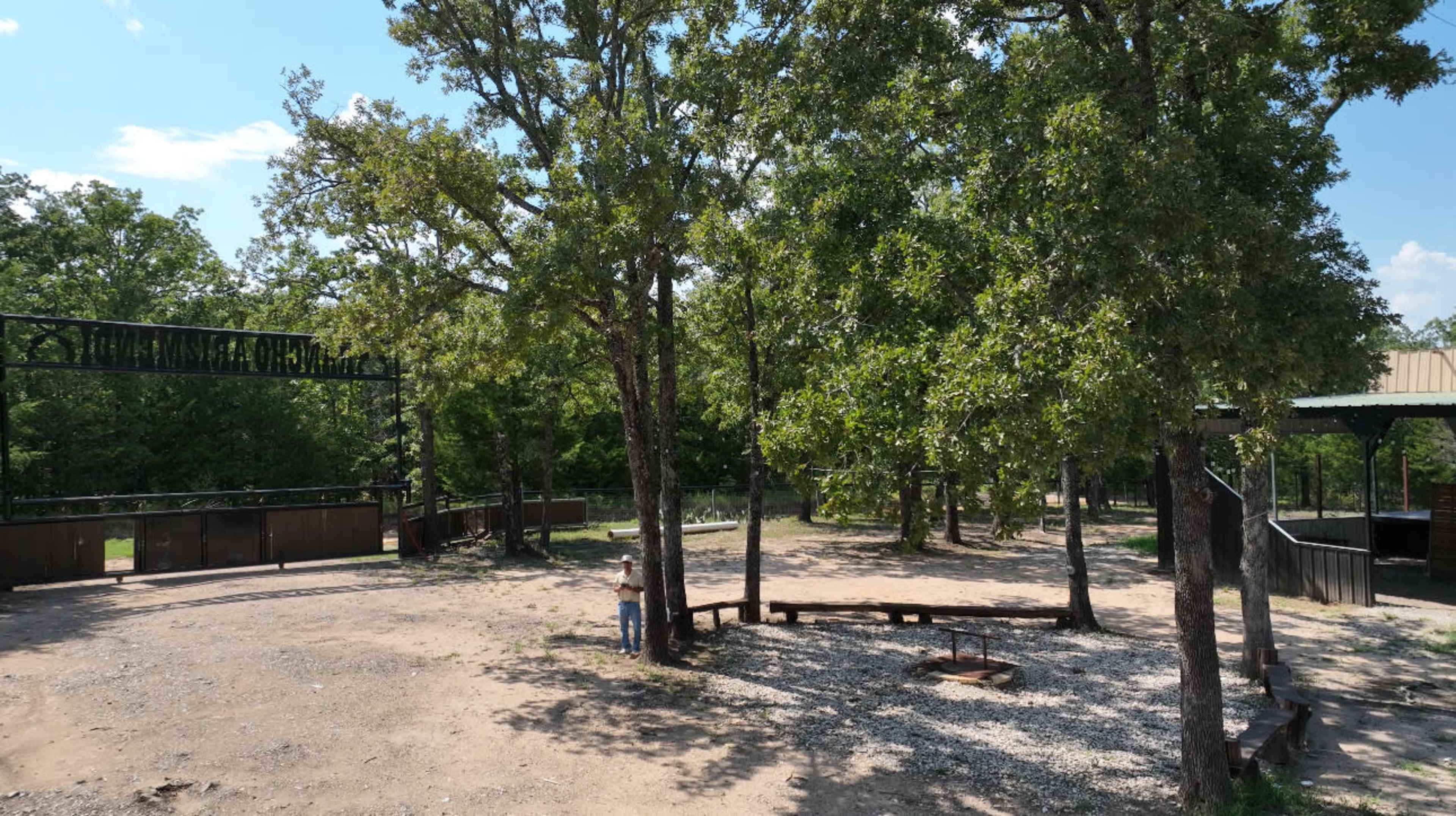 A cleared area with scattered gravel and a fire pit is surrounded by trees and wooden structures.