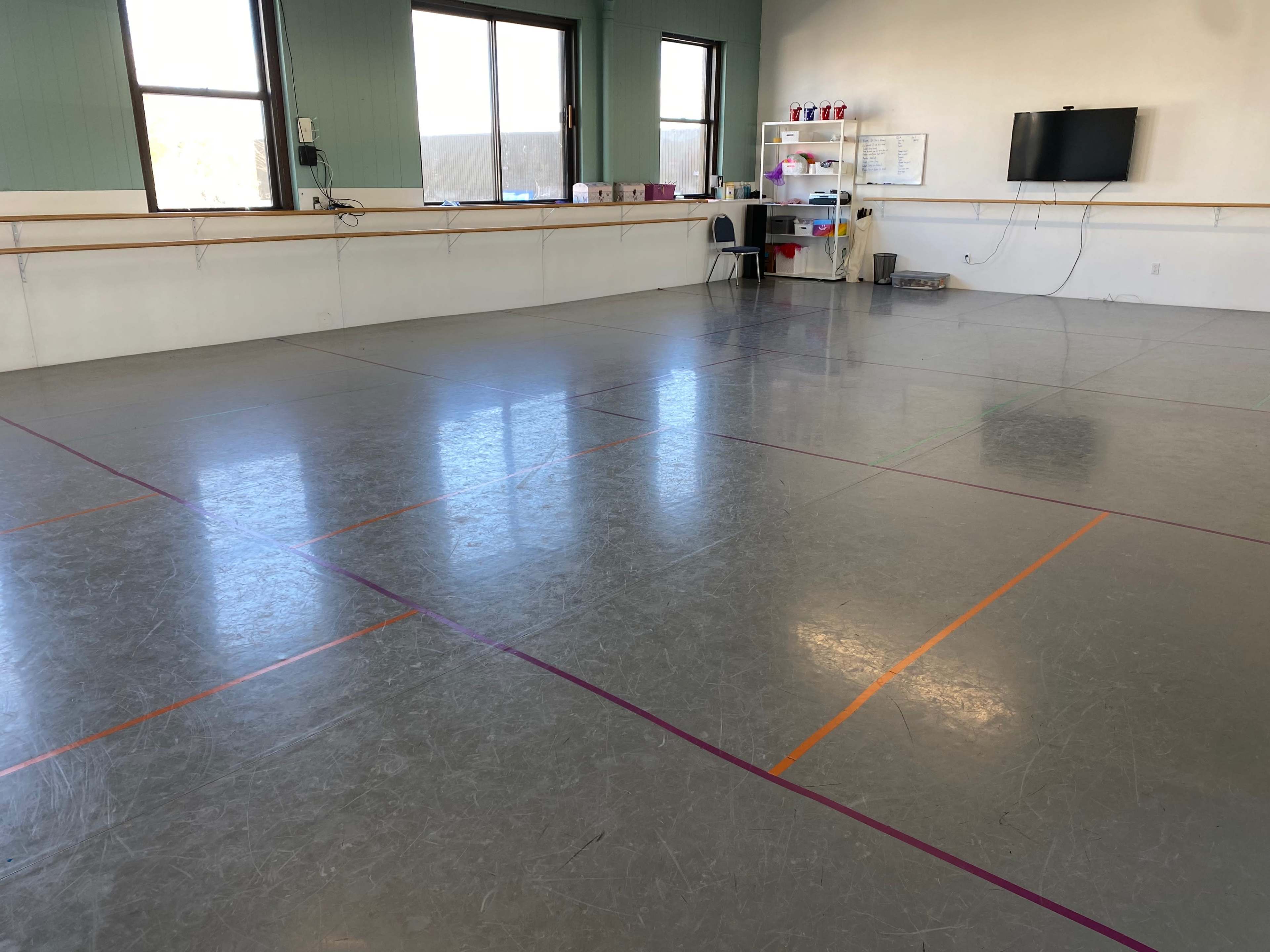 A spacious dance studio with a smooth floor marked by colored lines and a small seating area along one wall.