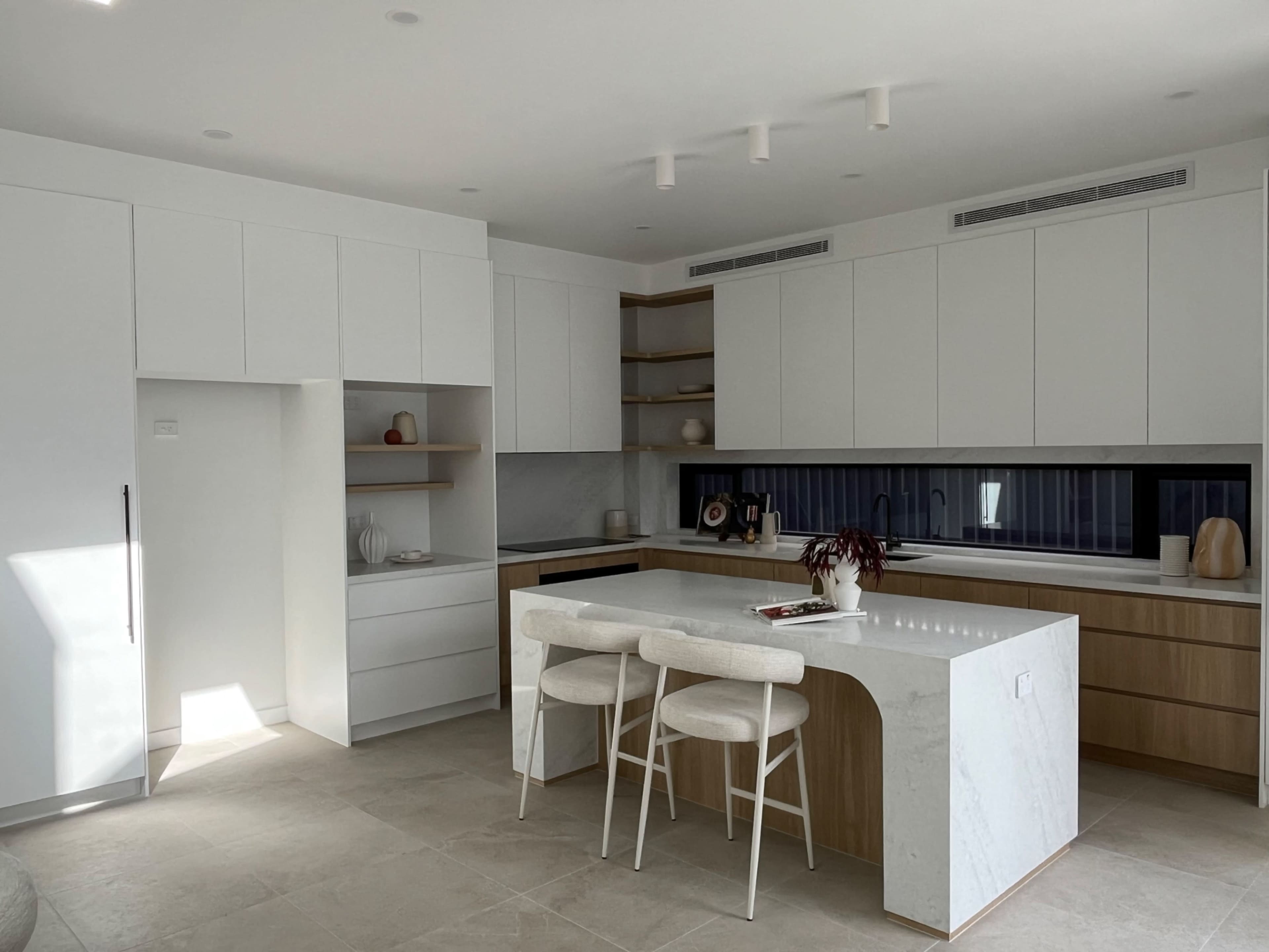 The image shows a modern kitchen with minimalist white cabinetry, a large island, and a neutral color palette.