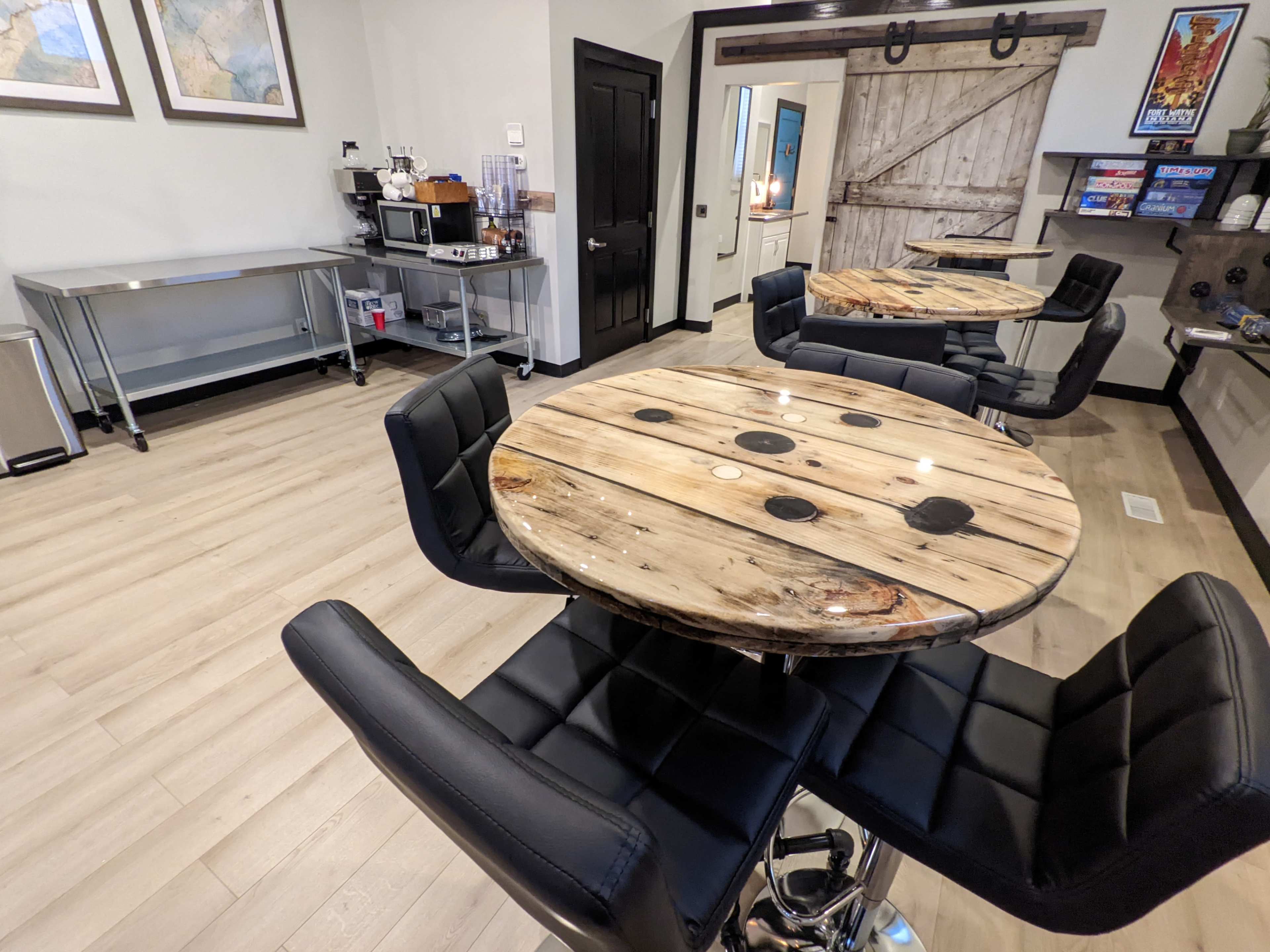 A modern room with two black leather chairs at round wooden tables featuring circular cutouts, and a metal serving table in the background.