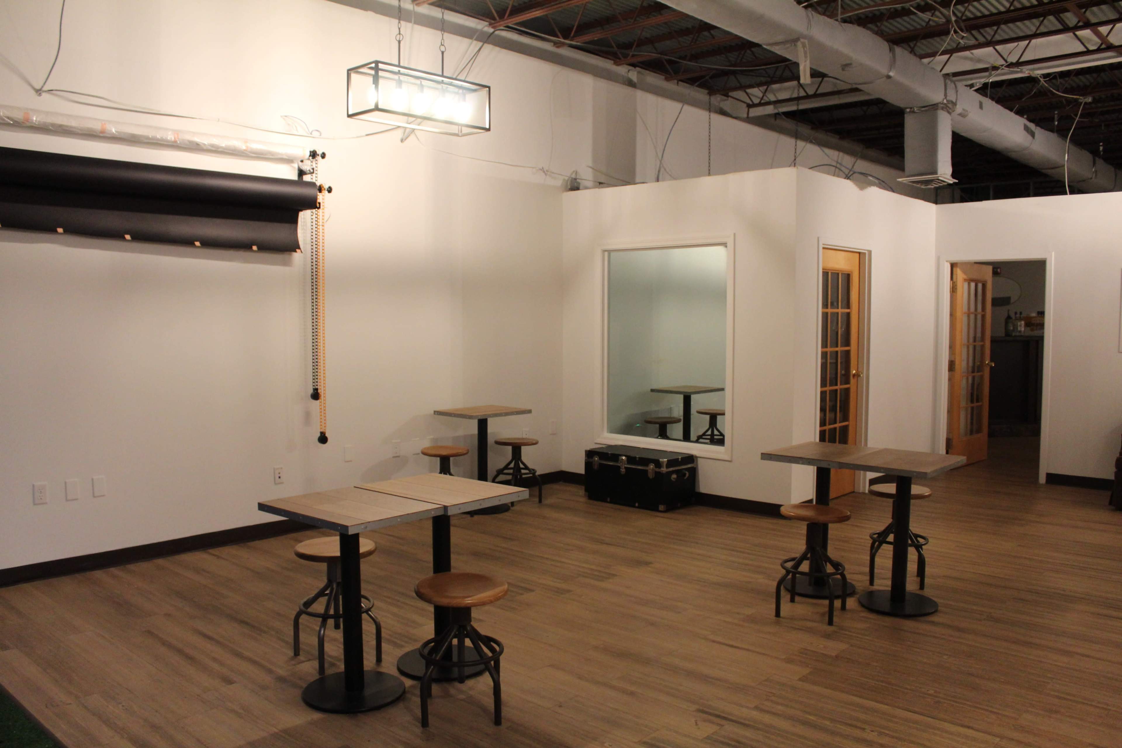 A sparsely furnished room with wooden tables and stools, a large mirror, and a ceiling light fixture.