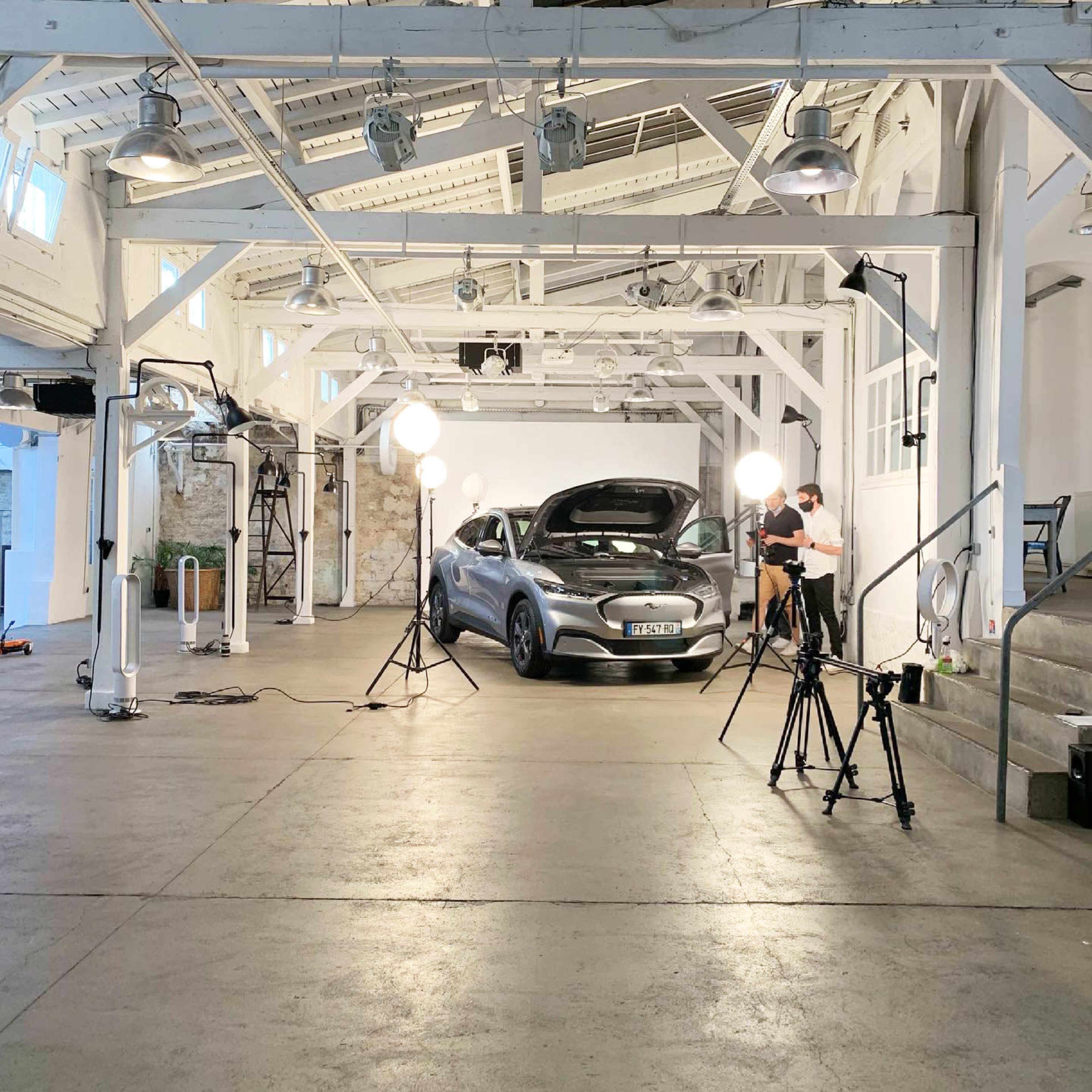 A modern studio space with a car prominently displayed under bright lights and several cameras set up for a photoshoot.