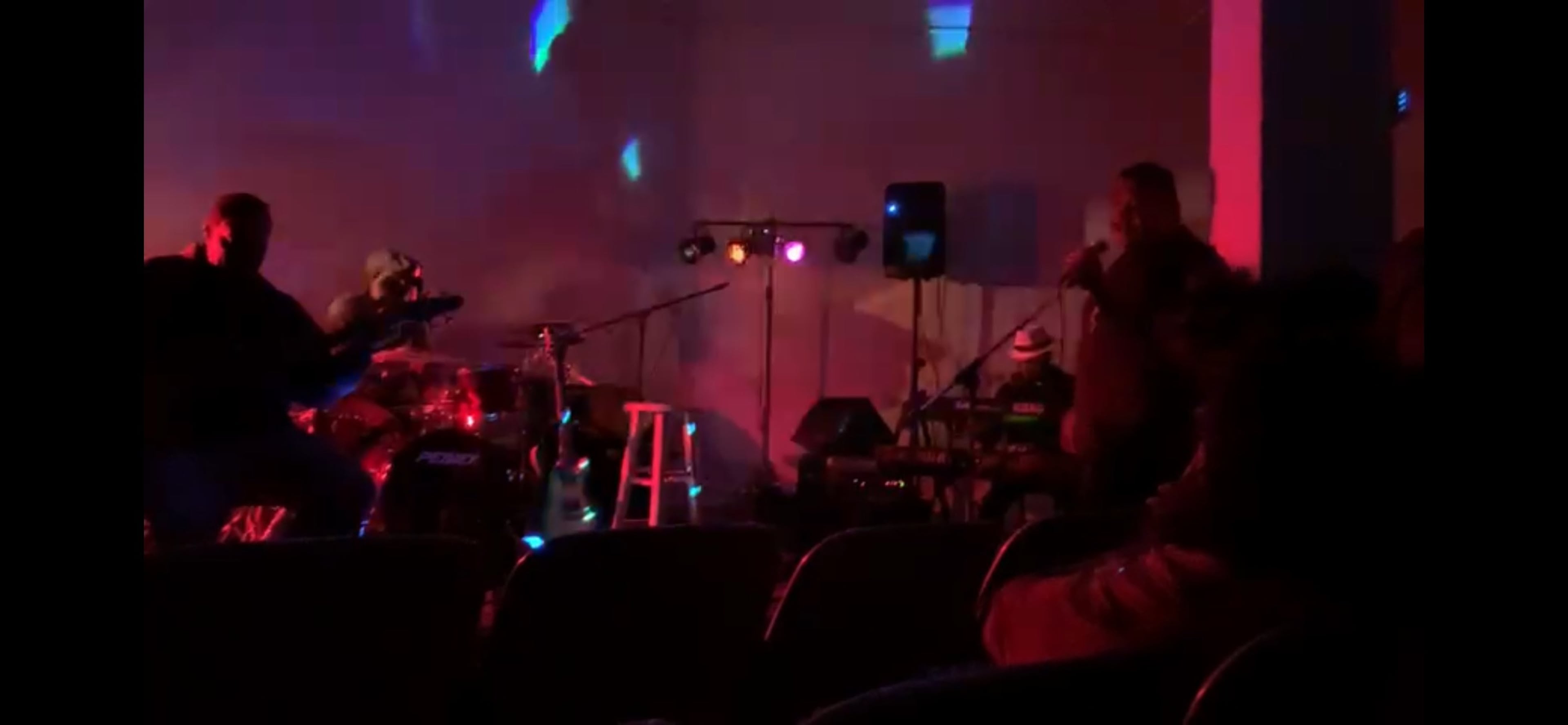 A band performs on stage while an audience watches from their seats in a dimly lit venue.