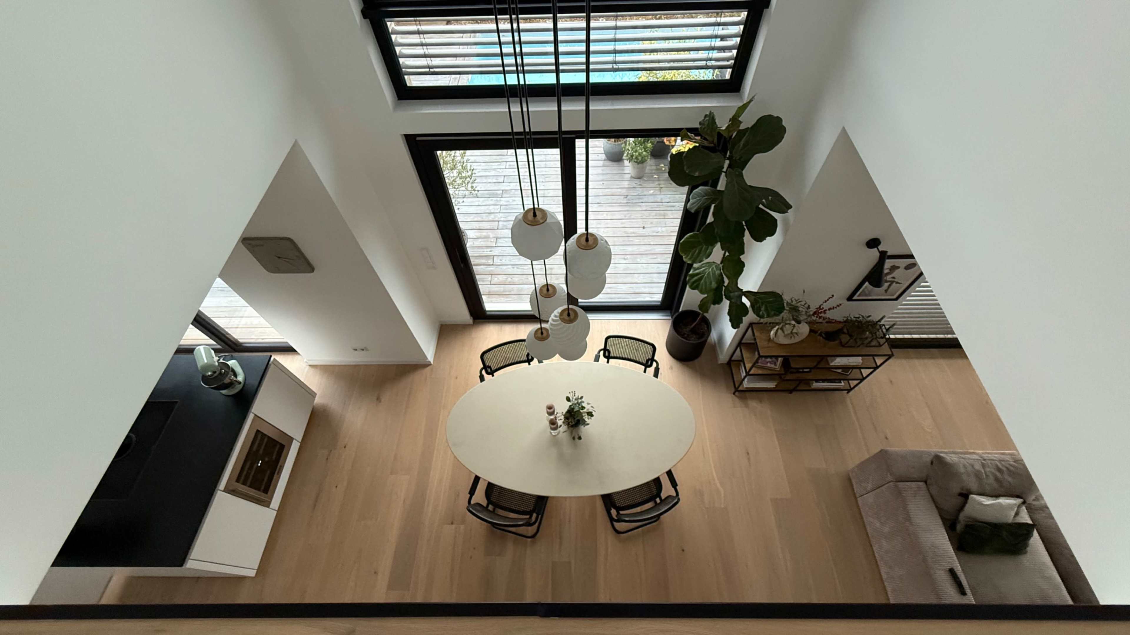 A modern dining area features a round table surrounded by chairs, with large windows allowing light to flow in and a view of an outdoor patio.