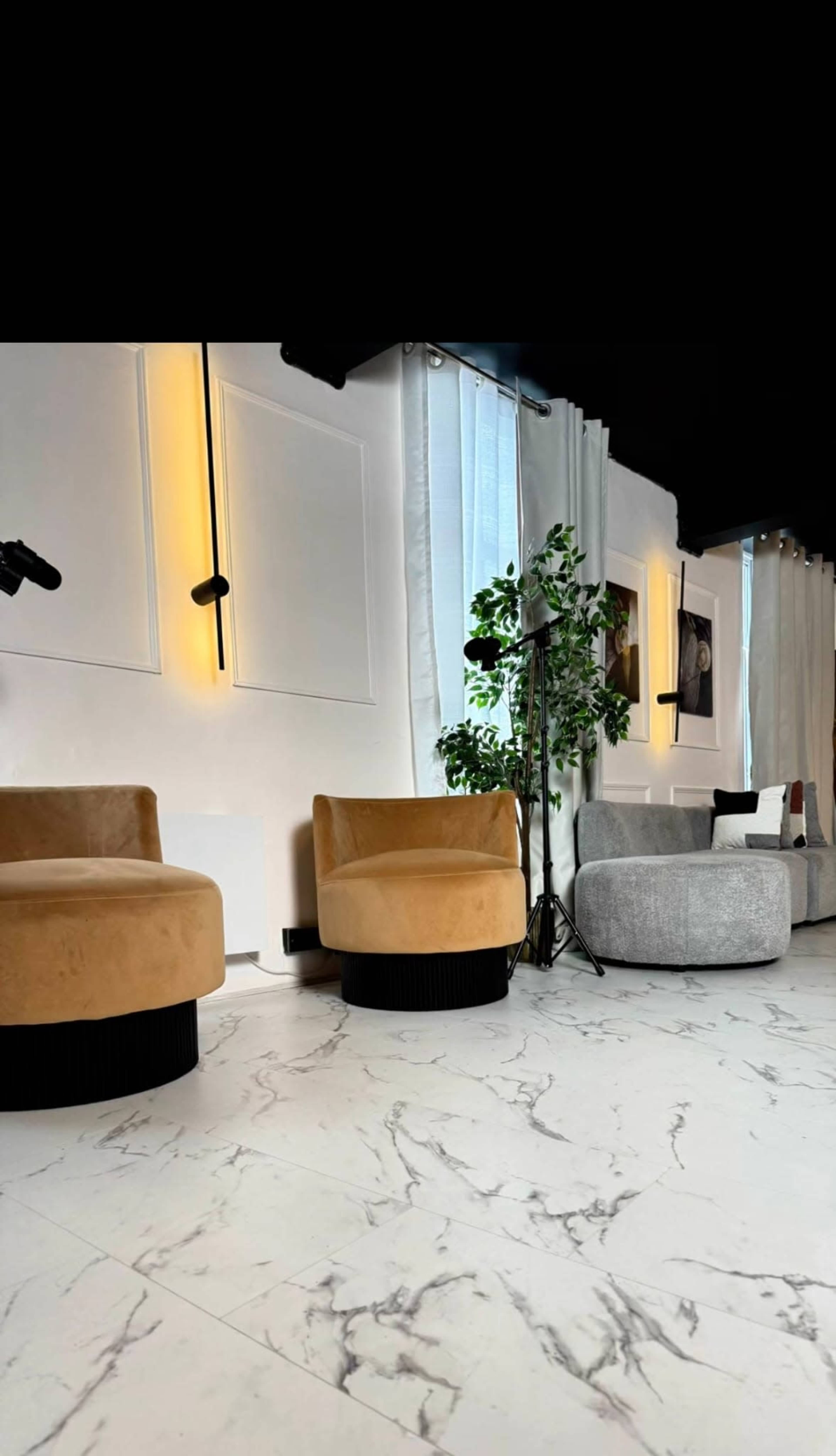 The image features a stylish interior with two plush chairs, a gray sofa, and large windows draped with curtains, set against a marble-patterned floor.