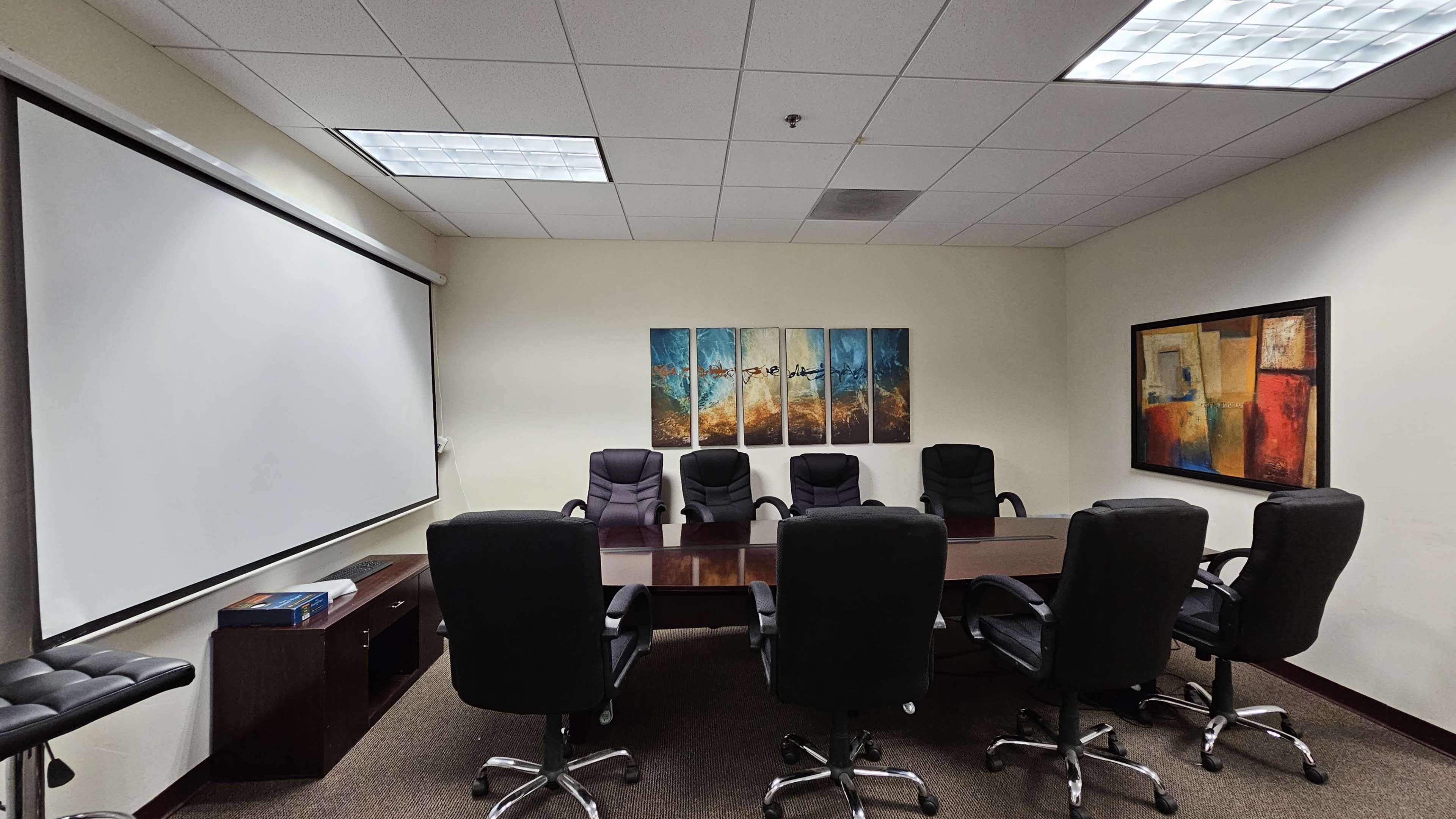 A conference room with a large wooden table surrounded by black chairs, and artwork displayed on the walls.
