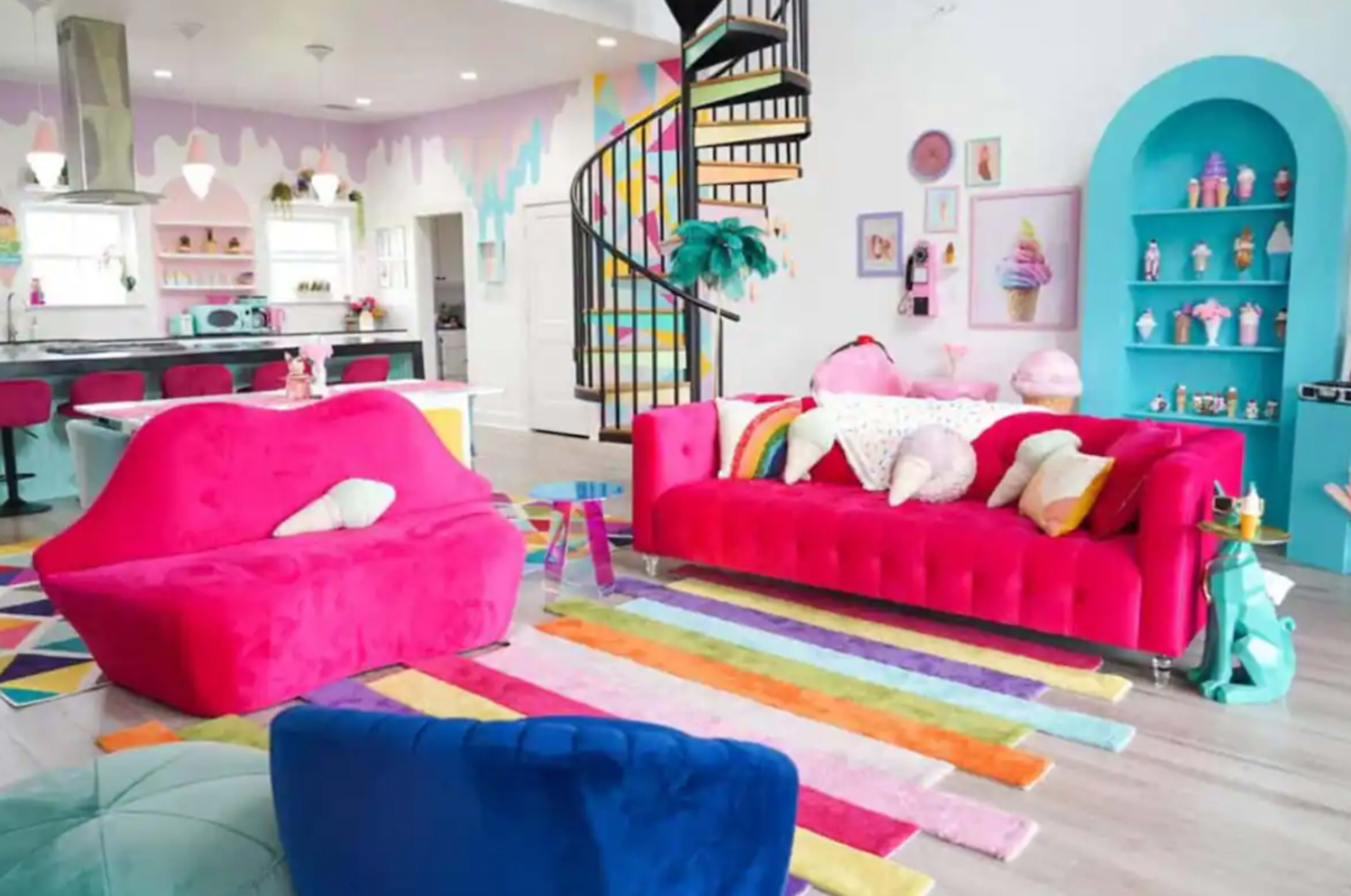 A brightly decorated living room with pink sofas, a colorful rug, and a spiral staircase leading to an upper level.