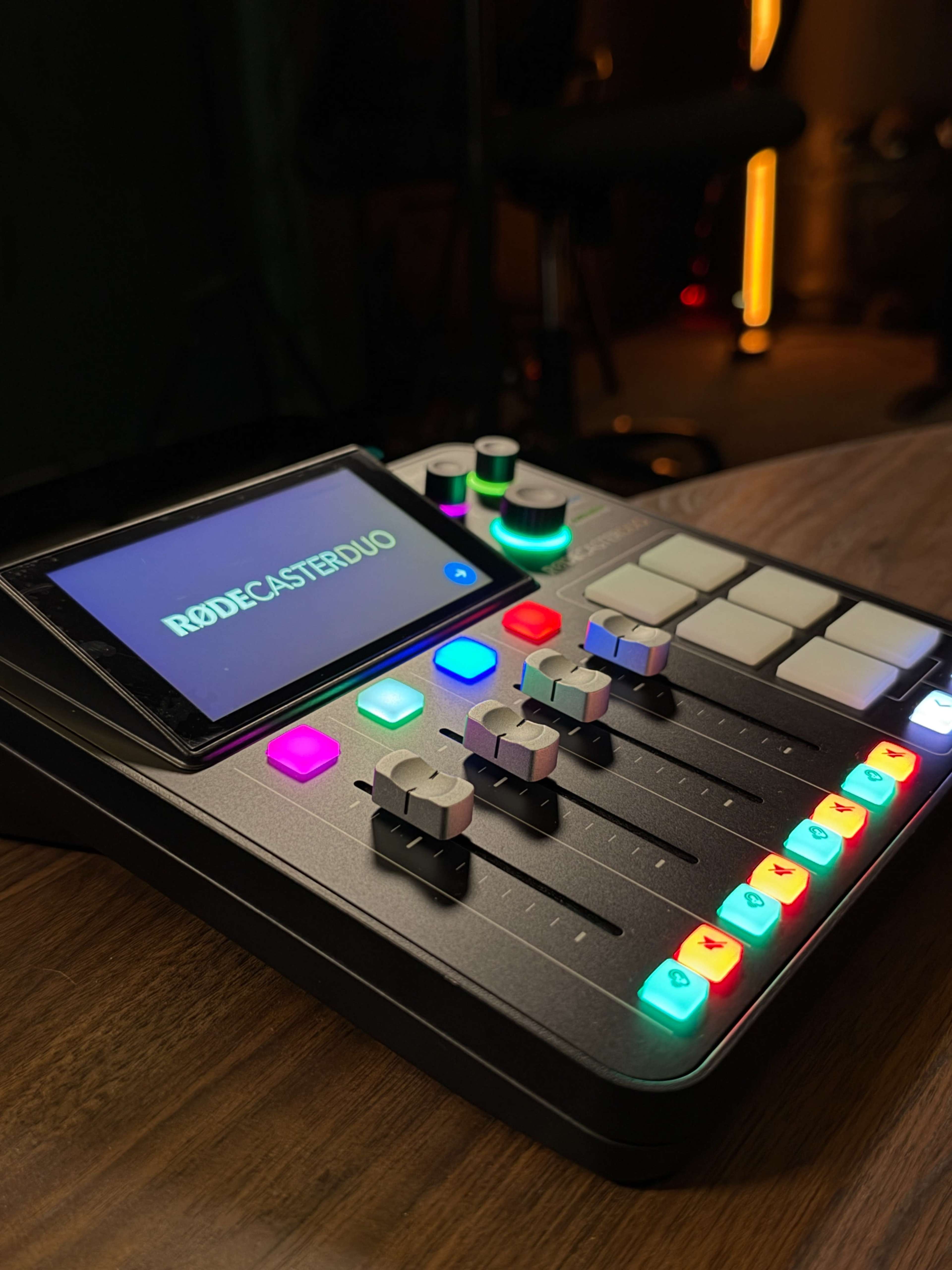A Rodecaster Pro II audio mixing console is displayed on a wooden surface, featuring multicolored buttons and sliders.