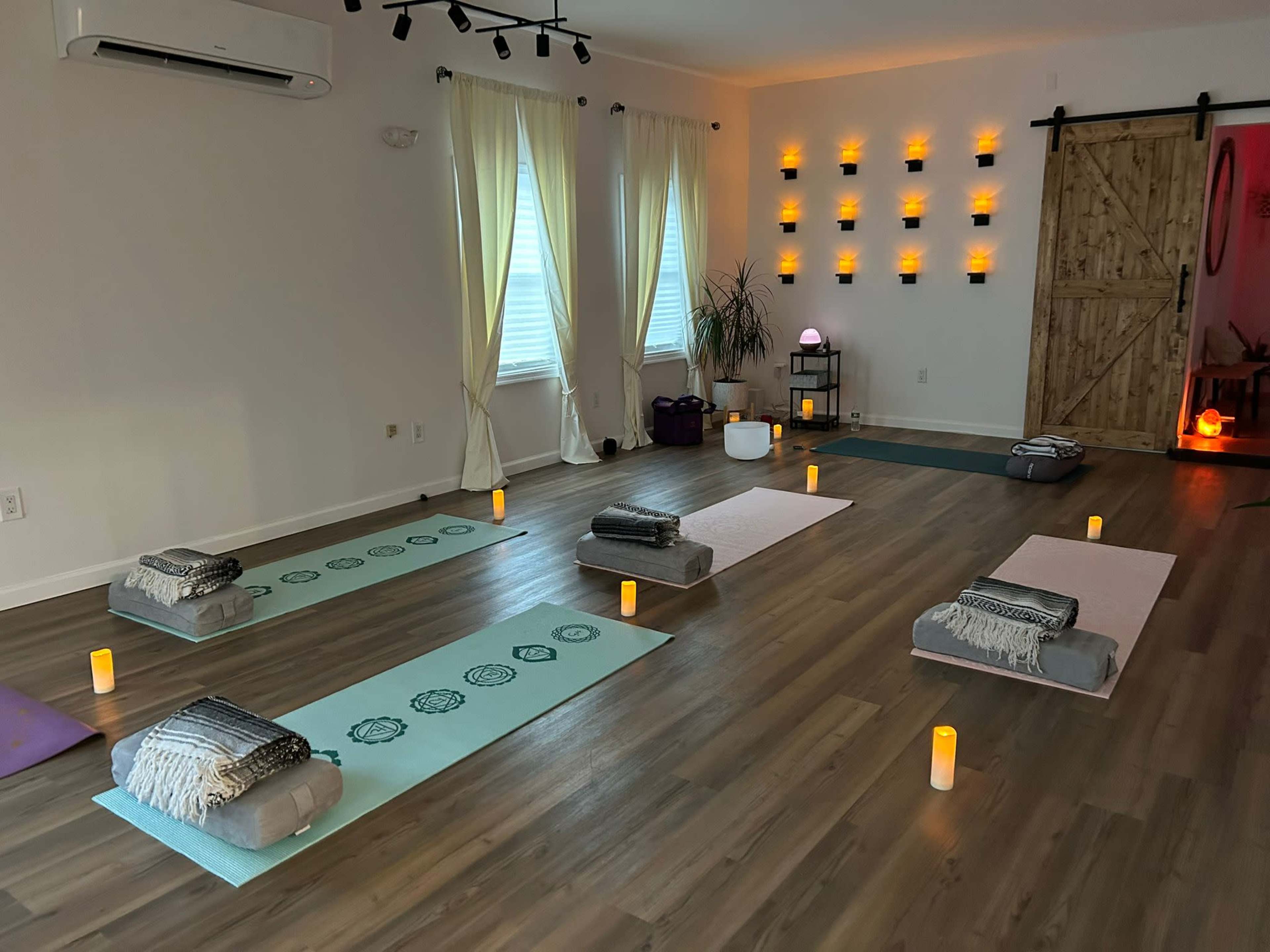 A serene yoga studio featuring several mats arranged in rows, surrounded by soft candlelight and decor on the walls.