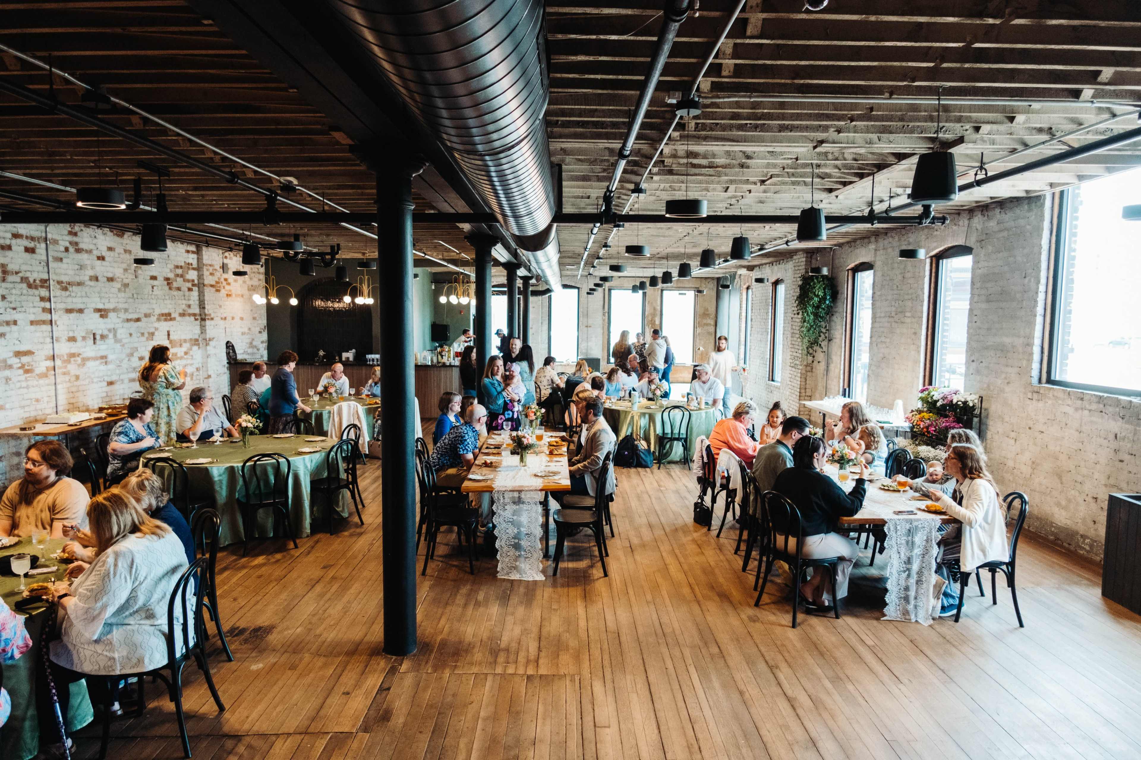 A spacious dining area with people seated at tables, engaged in conversation, and enjoying their meals in a well-lit venue with large windows.