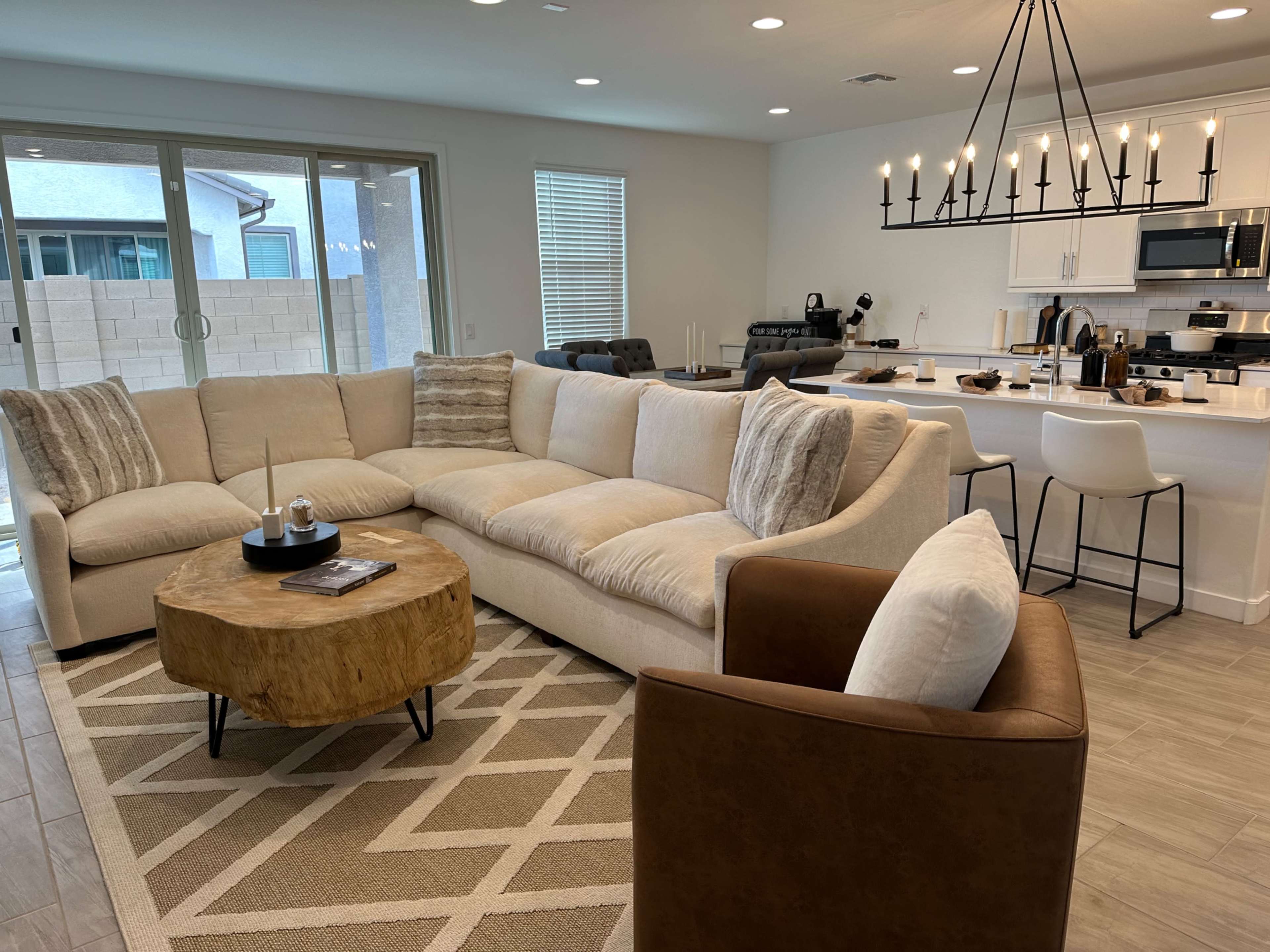 A modern living room with a large sectional sofa, a round wooden coffee table, and a kitchen area visible in the background.