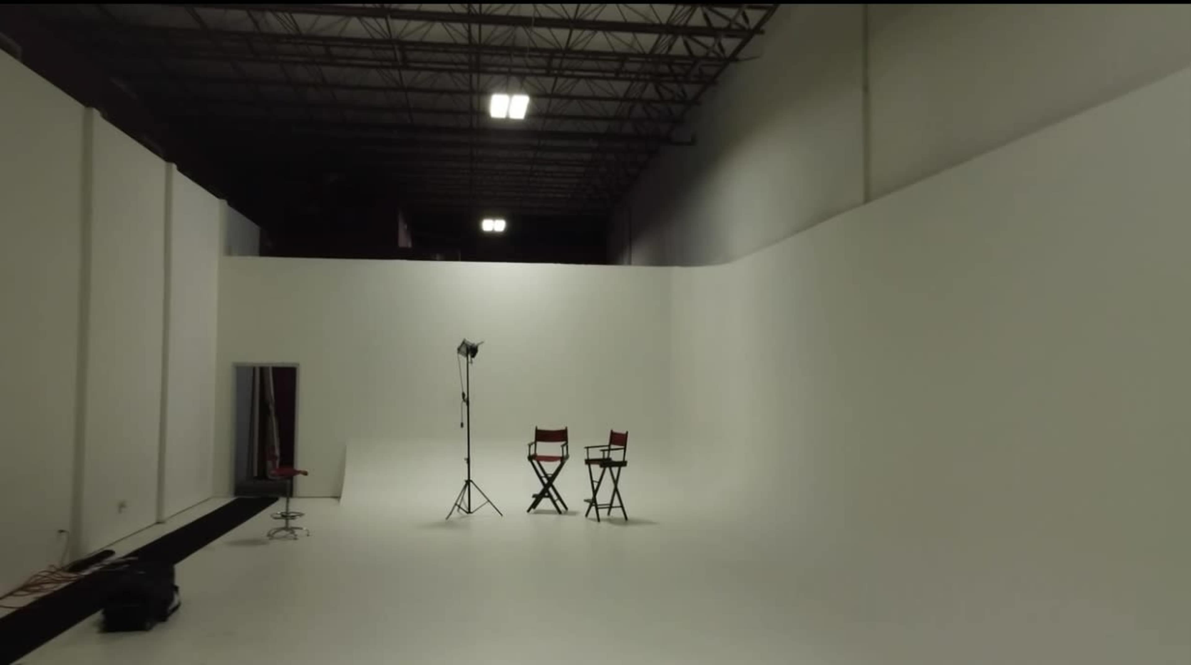 A sparse studio space features two red director's chairs and a single lighting stand set against a white backdrop.