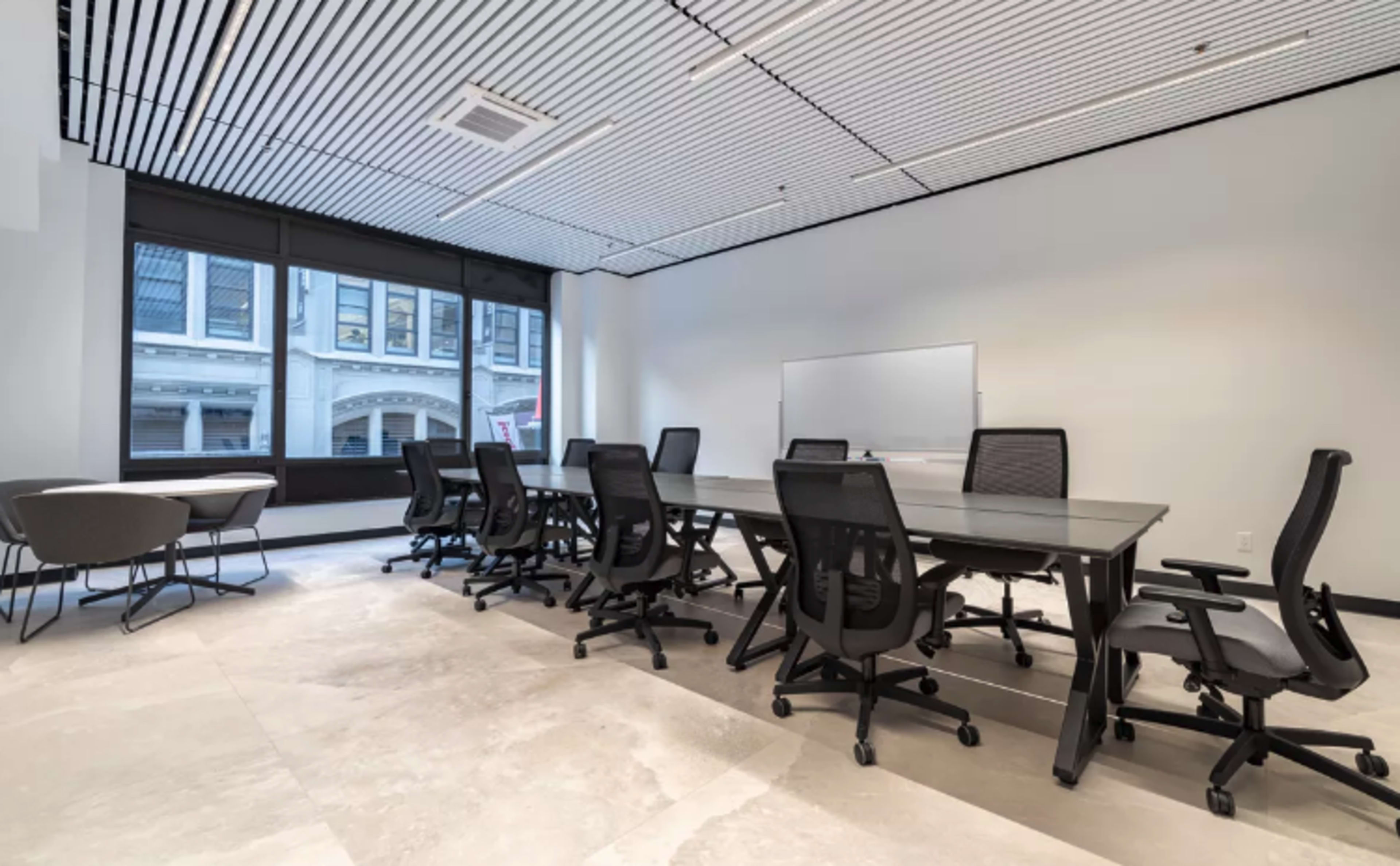 A modern conference room features a long glass table surrounded by ergonomic chairs, with large windows providing natural light.