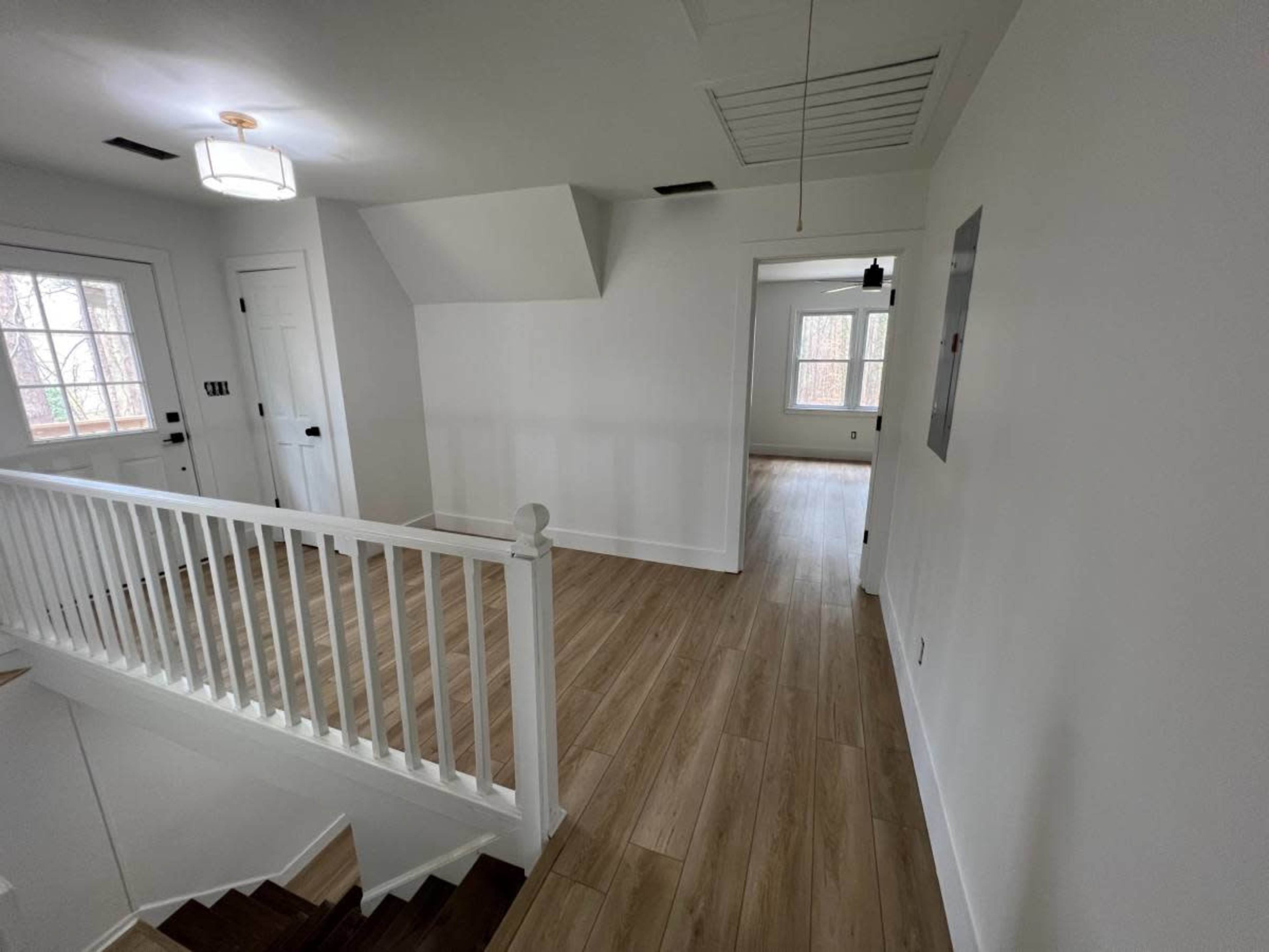 A well-lit hallway features a set of stairs leading down, surrounded by white walls and wooden flooring.