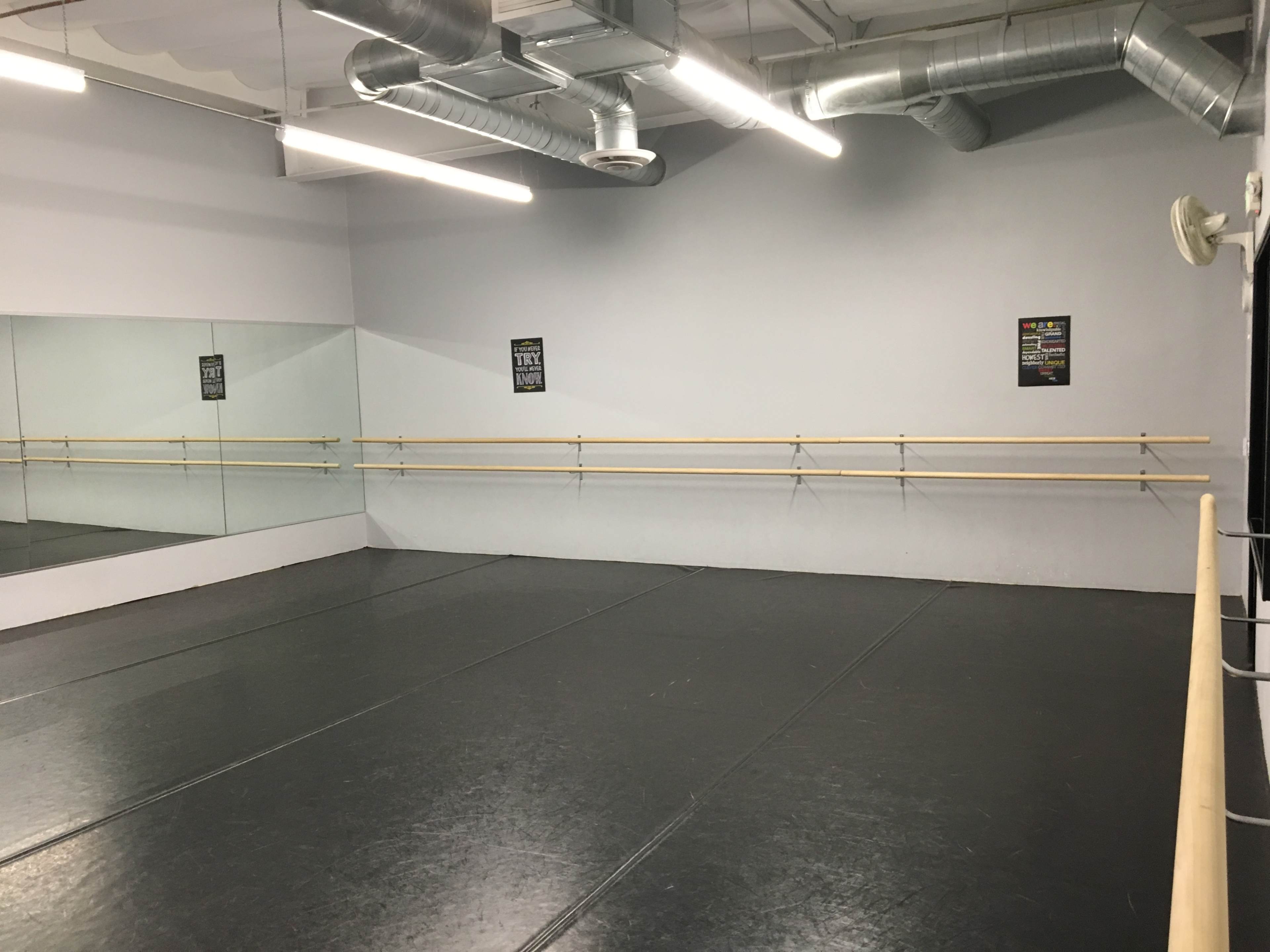 A spacious dance studio with a mirrored wall and wooden ballet bars along the perimeter.