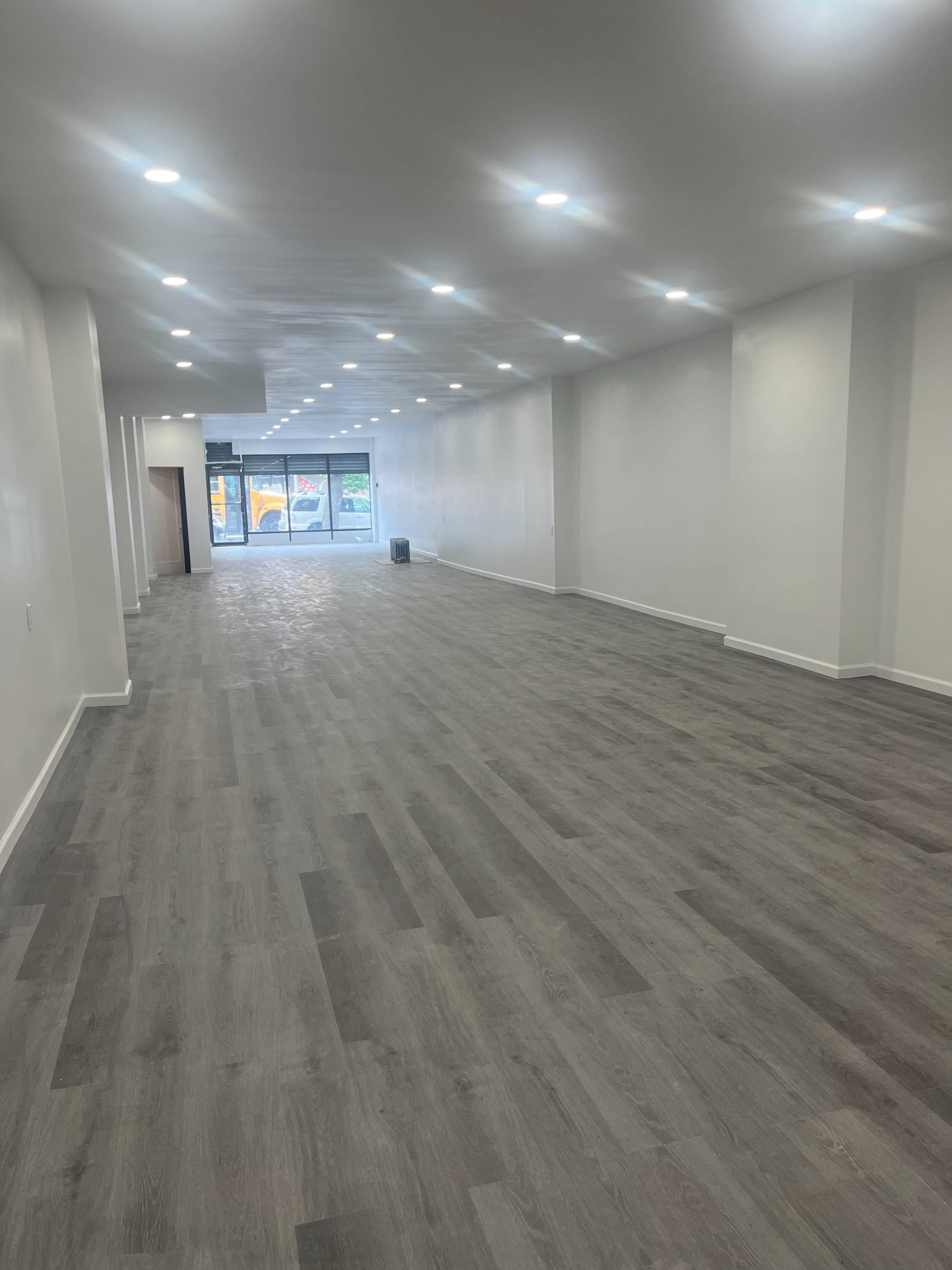 The image shows a spacious, empty retail space with gray flooring and bright overhead lights.