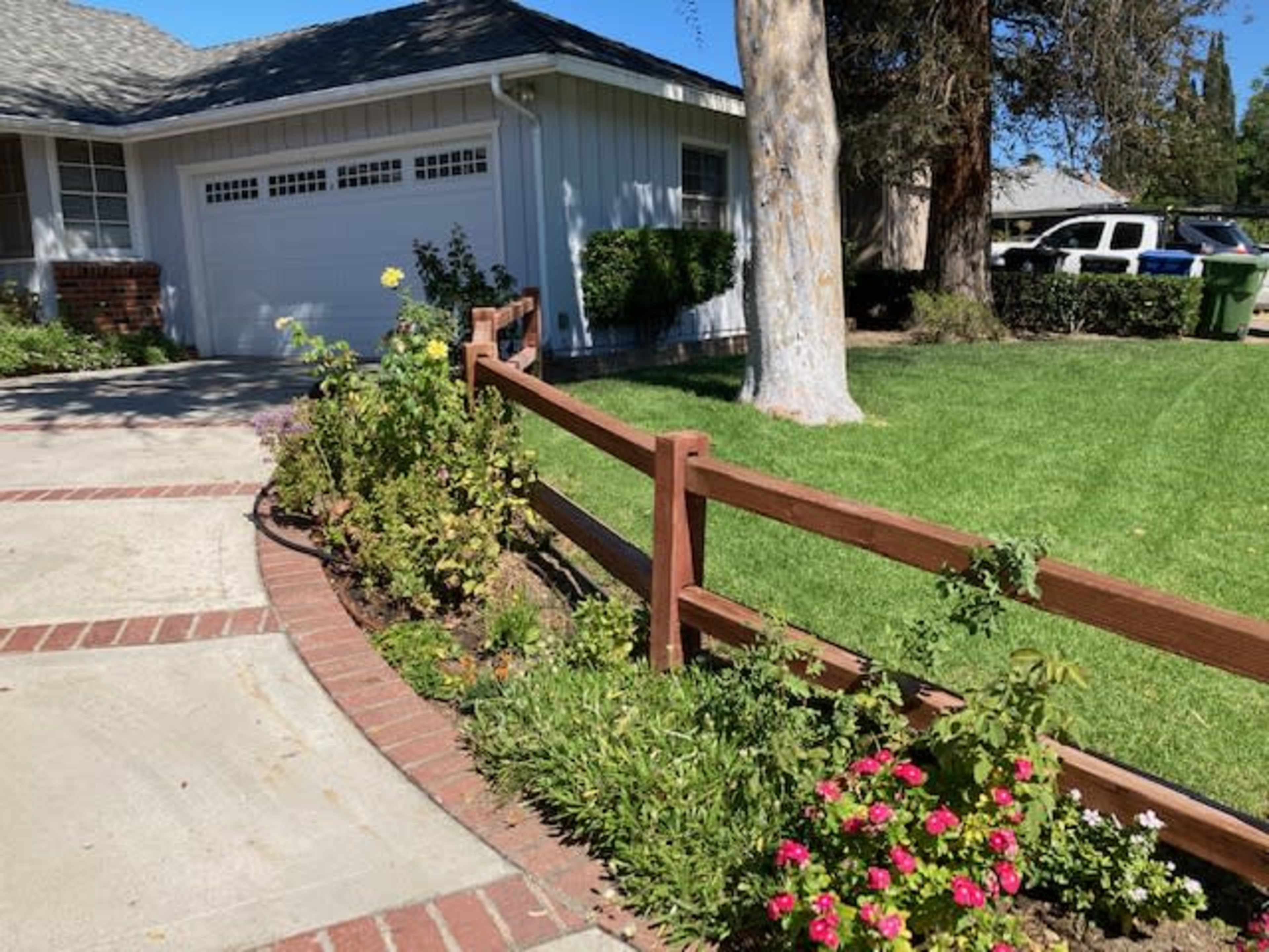 A neatly landscaped front yard with a wooden fence bordering a flower bed and a driveway leading to a garage.