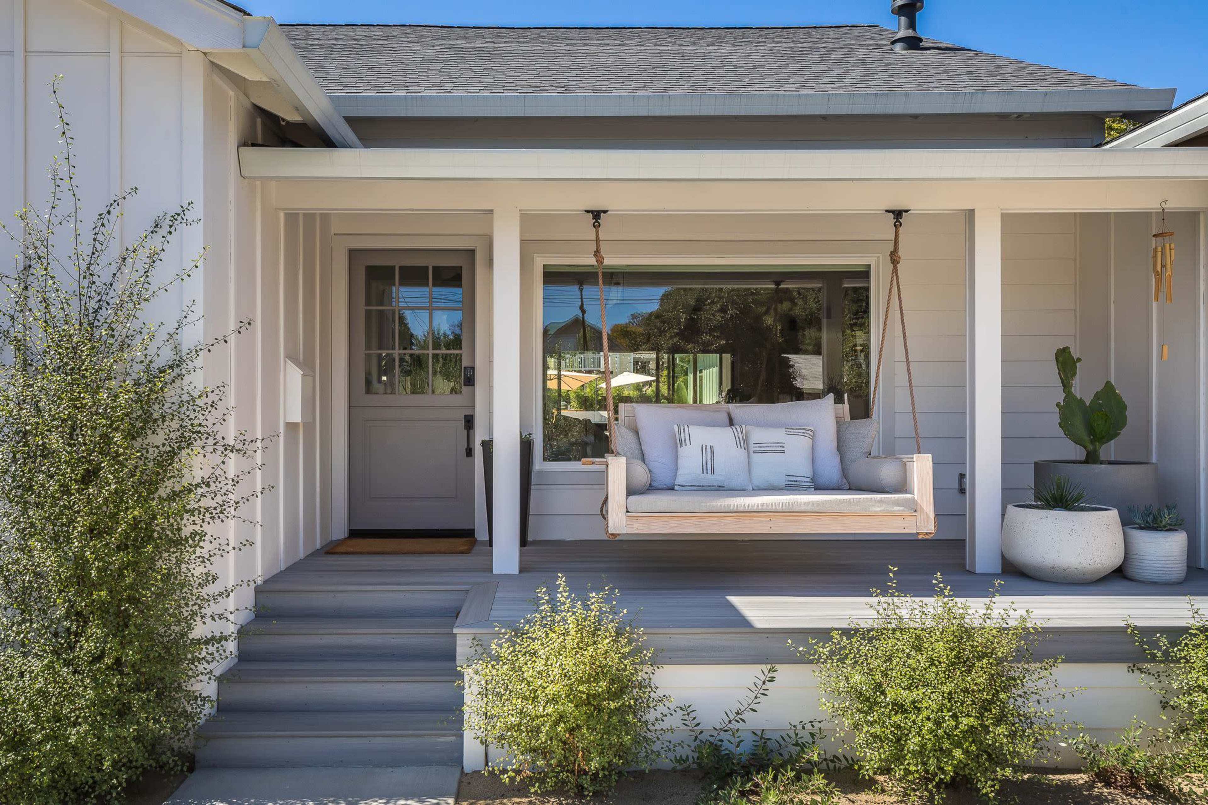 A front porch with a swing, a door, and potted plants.