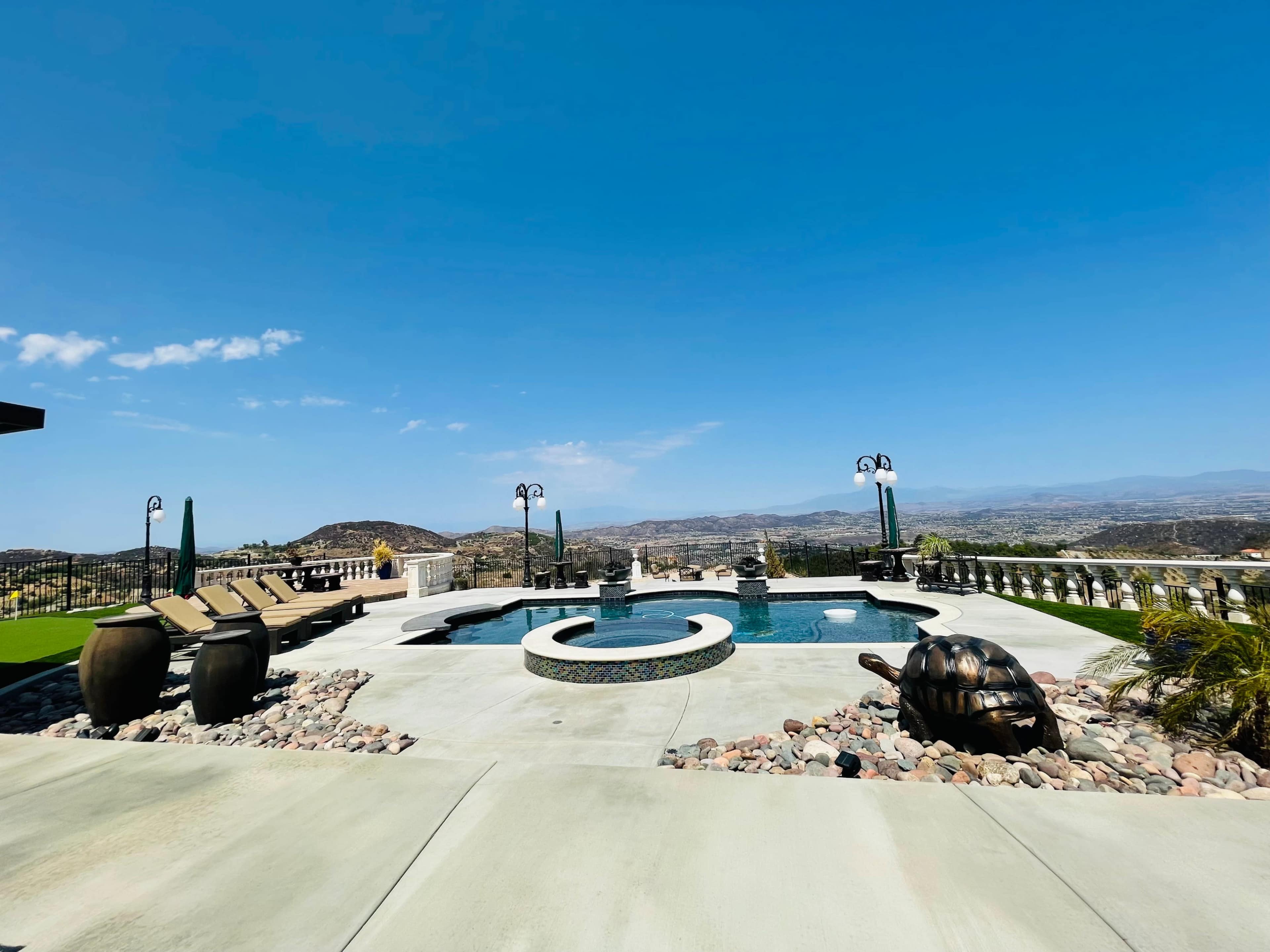 A spacious outdoor area featuring a swimming pool, lounge chairs, and a panoramic view of distant hills under a clear blue sky.