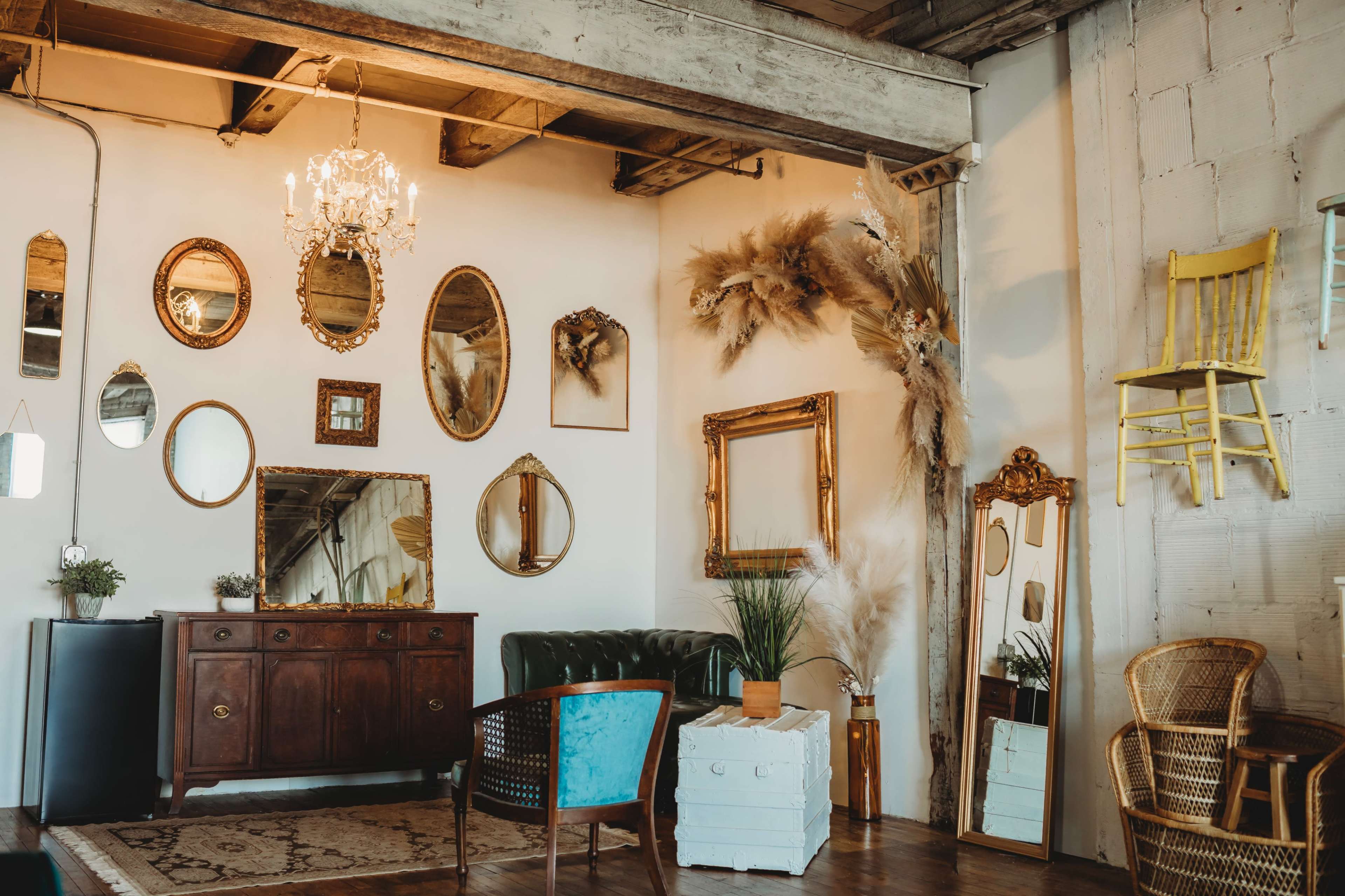 A stylish interior featuring a green leather sofa, an assortment of decorative mirrors on the wall, and various furniture pieces, including a wooden cabinet and a wicker chair.