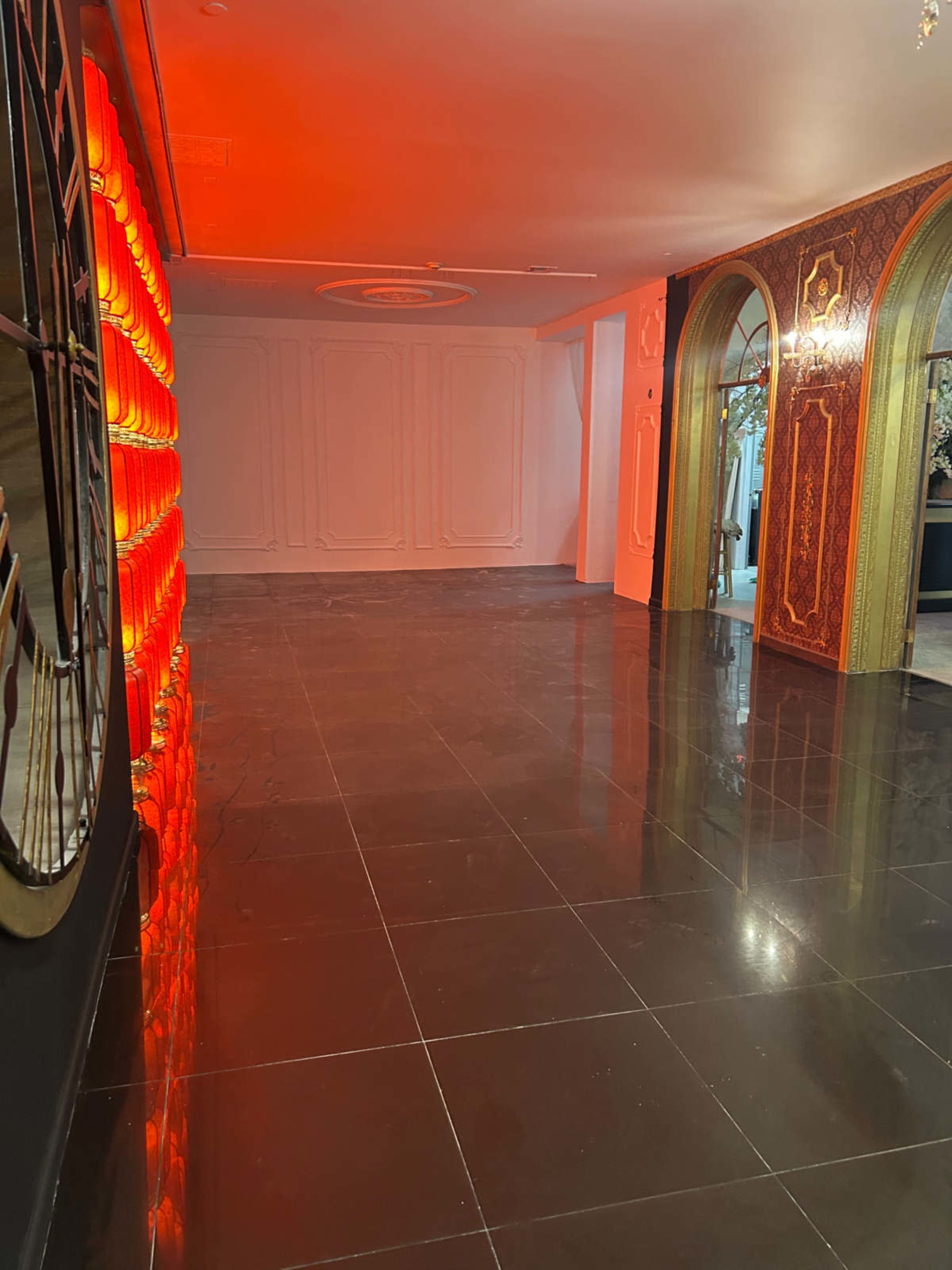 The image shows an empty indoor space with polished black tile flooring and red lighting creating a warm ambiance.