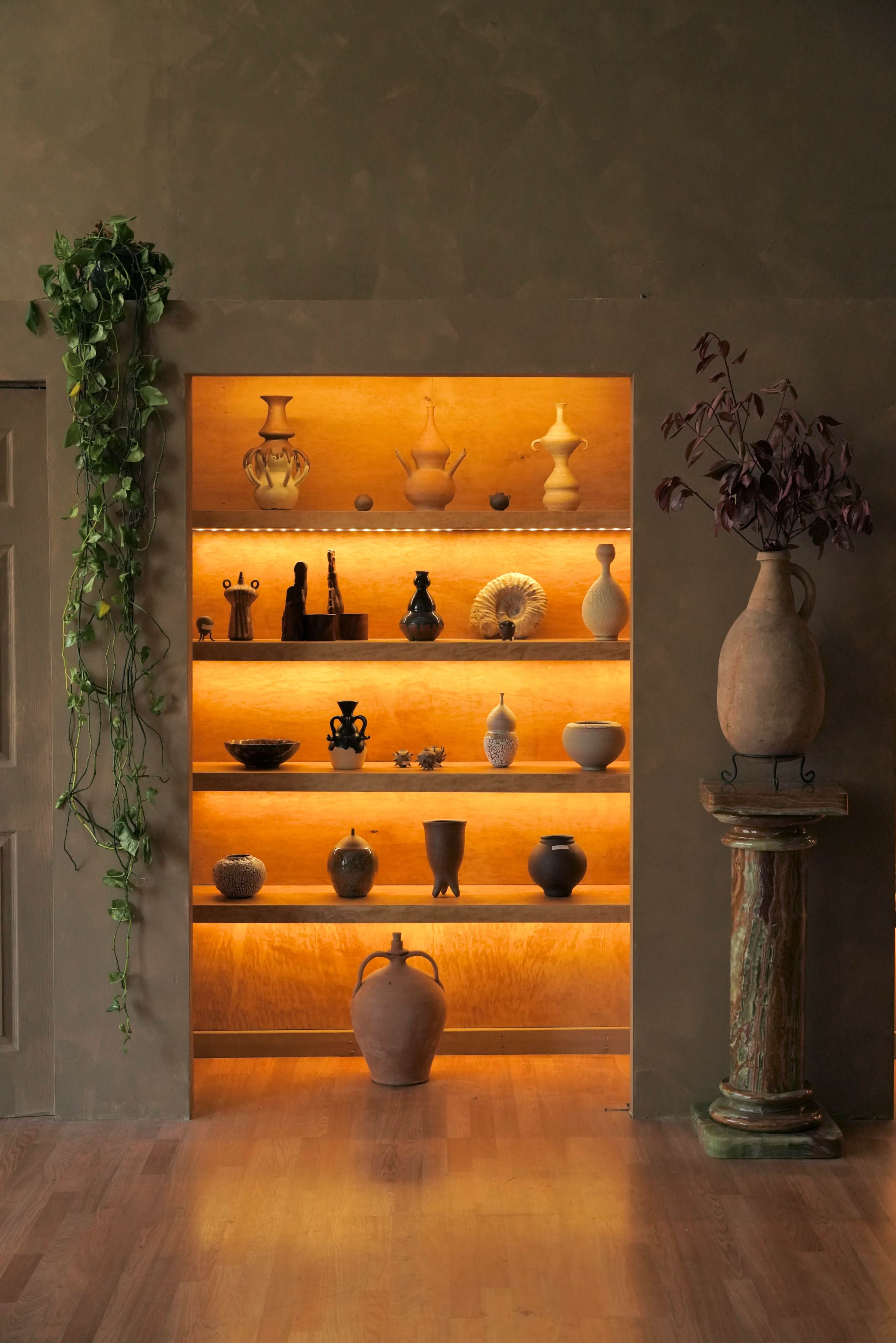 A well-lit display shelf featuring various ceramic vases and pots against a textured wall.