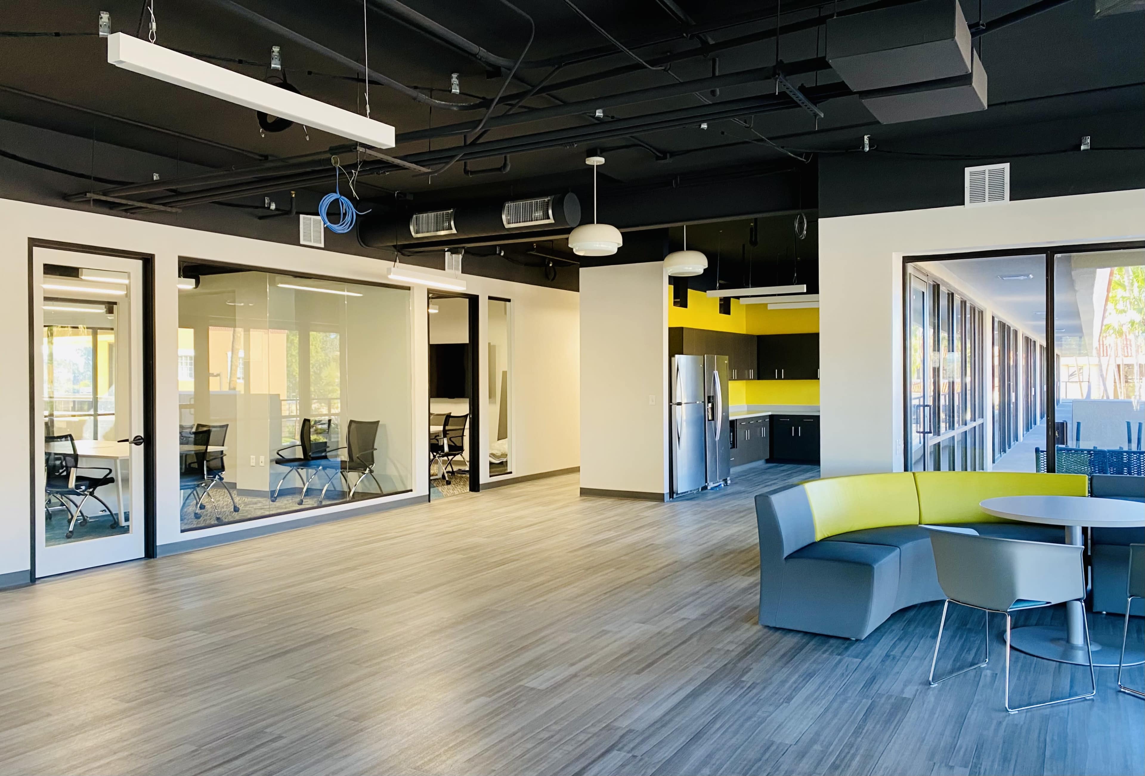 A modern office space with glass-walled meeting rooms, a kitchenette area, and a seating arrangement featuring a curved sofa.